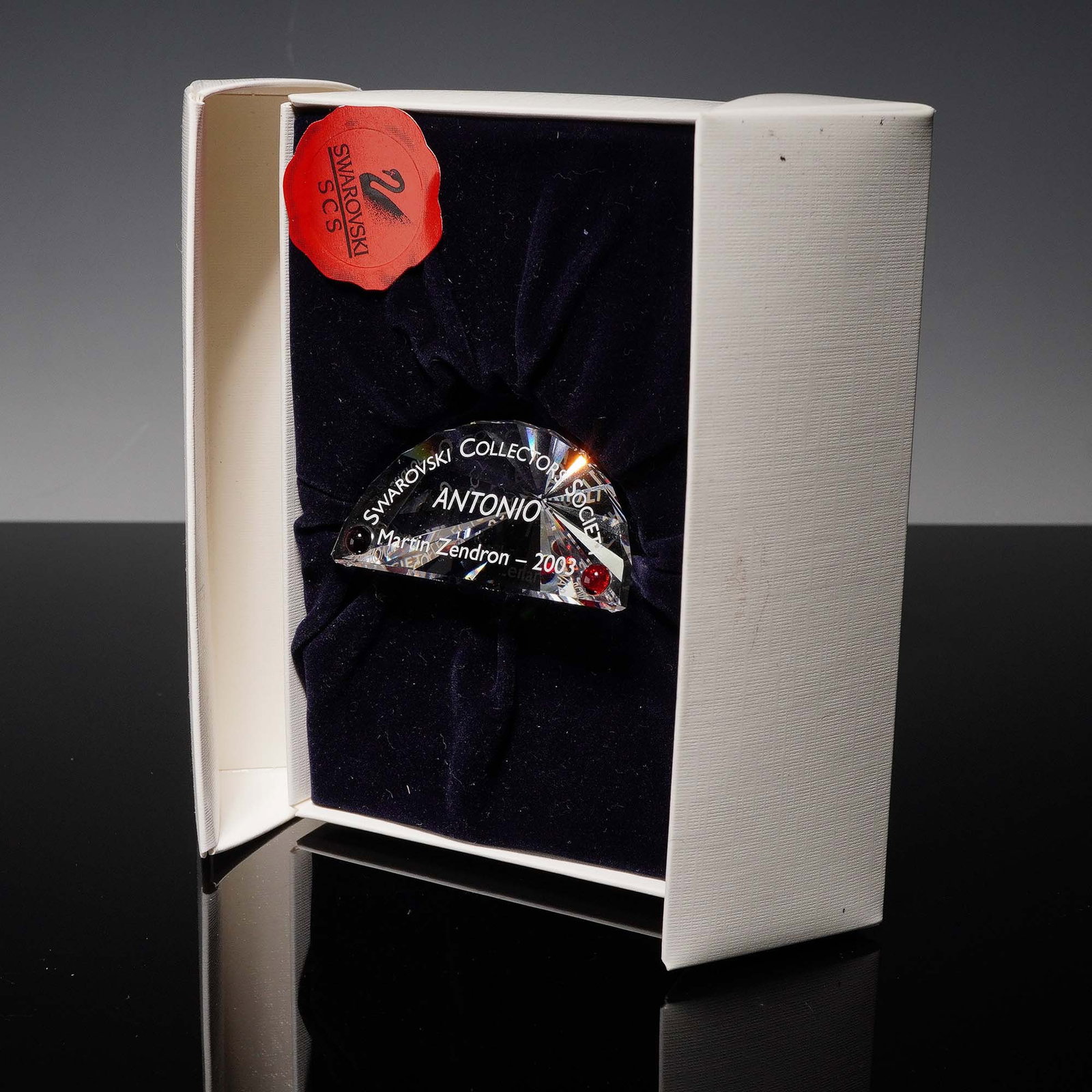 Swarovski Crystal Collector Society Plaque, Antonio: Presented is a Swarovski Collector Society (SCS) plaque titled "Antonio," crafted by Martin Zendron in 2003. The plaque is designed in clear crystal with red crystal accents, featuring an engraved SCS