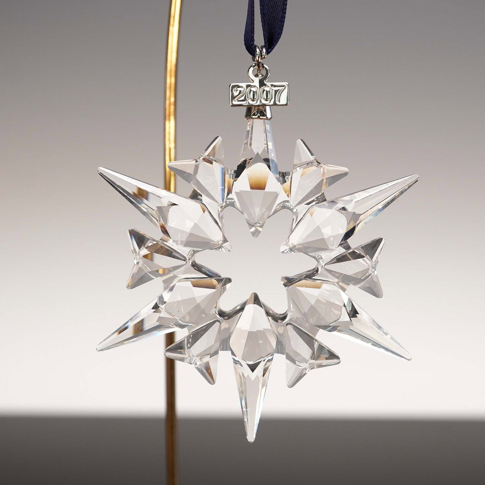Swarovski Crystal 2007 Christmas Ornament: Lead crystal annual limited edition tree ornament. Clear snowflake shaped crystal ornament with blue satin ribbon. Finished with a metal tag with 2007 etched on it. Swarovski backstamp. This item has 