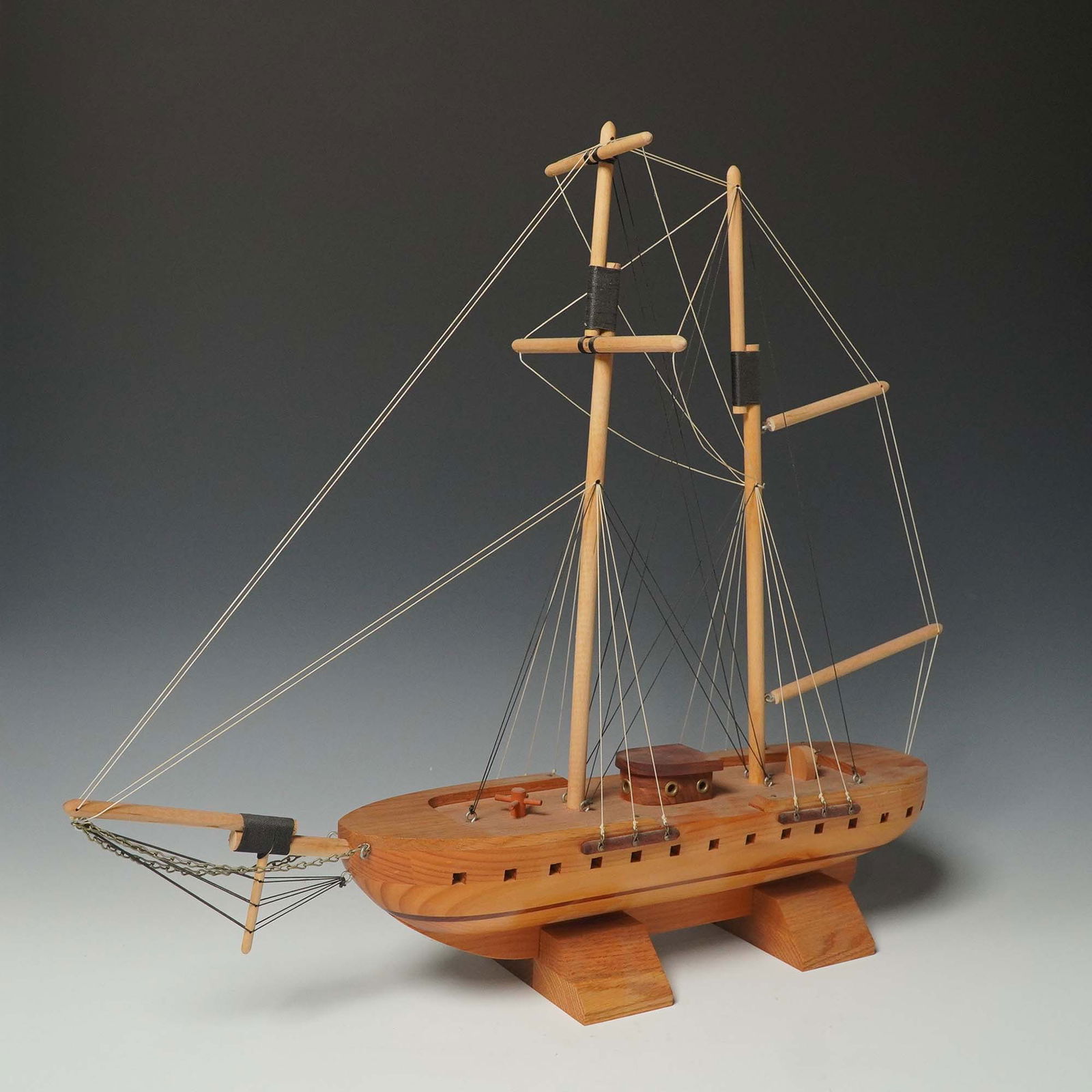 Wood Model Sailing Ship, Two-Mast Display with Base: Handcrafted wooden model ship featuring a two-mast rig with intricate string rigging, chain accents, and a hull with carved port details. The deck includes a raised cabin with faux portholes and a sma