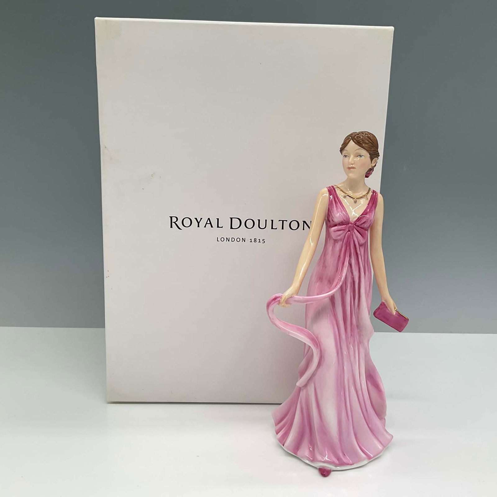 Royal Doulton Figurine, Julia HN5664: Elegant Royal Doulton figurine titled Julia, model HN5664, crafted from hand-decorated bone china. Featuring a graceful woman in a flowing pink evening gown with a matching clutch, this piece embodies