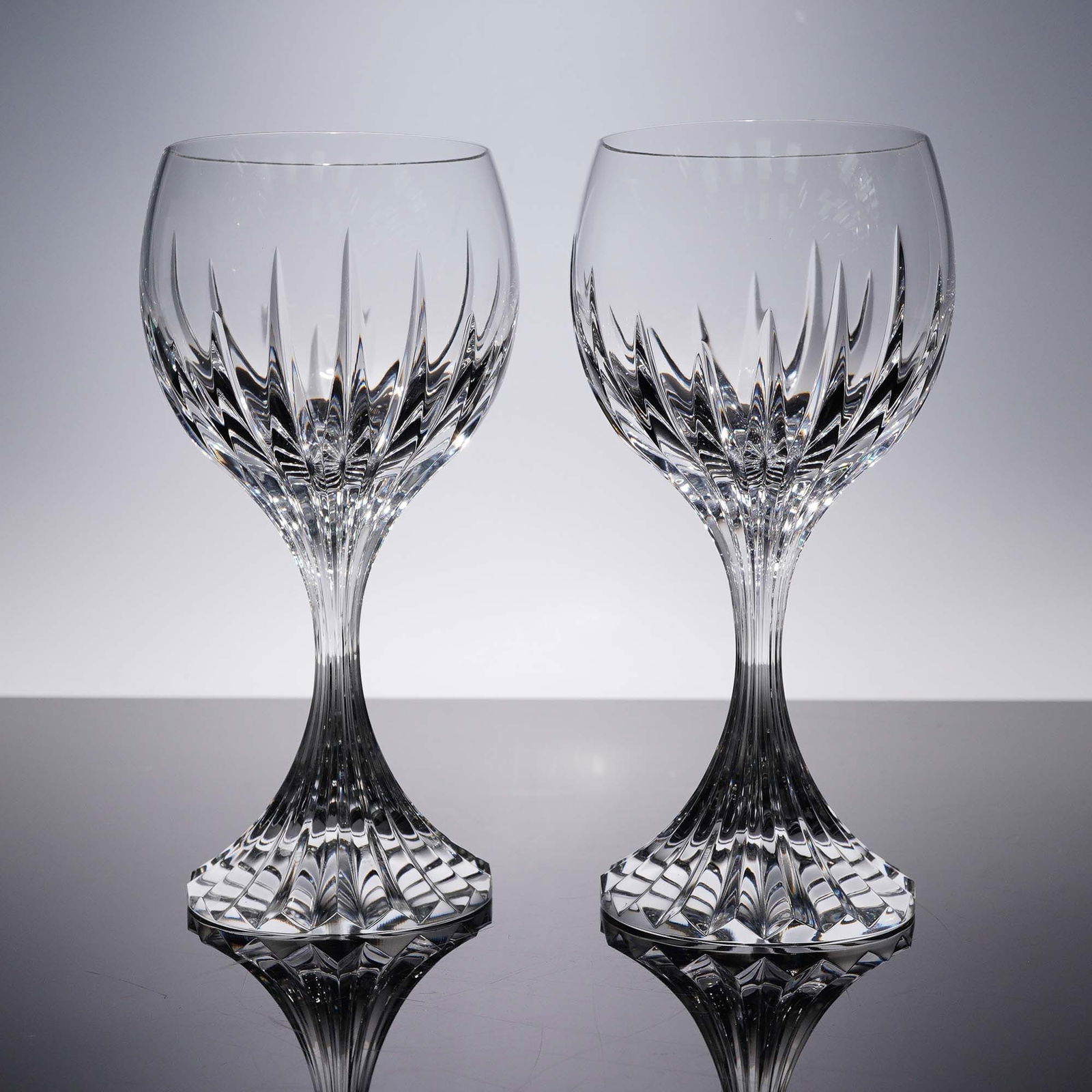 Pair of Baccarat Crystal Water Goblets, Massena: Each goblet features vertical cuts on the bowl that radiate downwards, creating a striking interplay of light and shadow. The stem has a flared, faceted base that enhances the overall design with adde