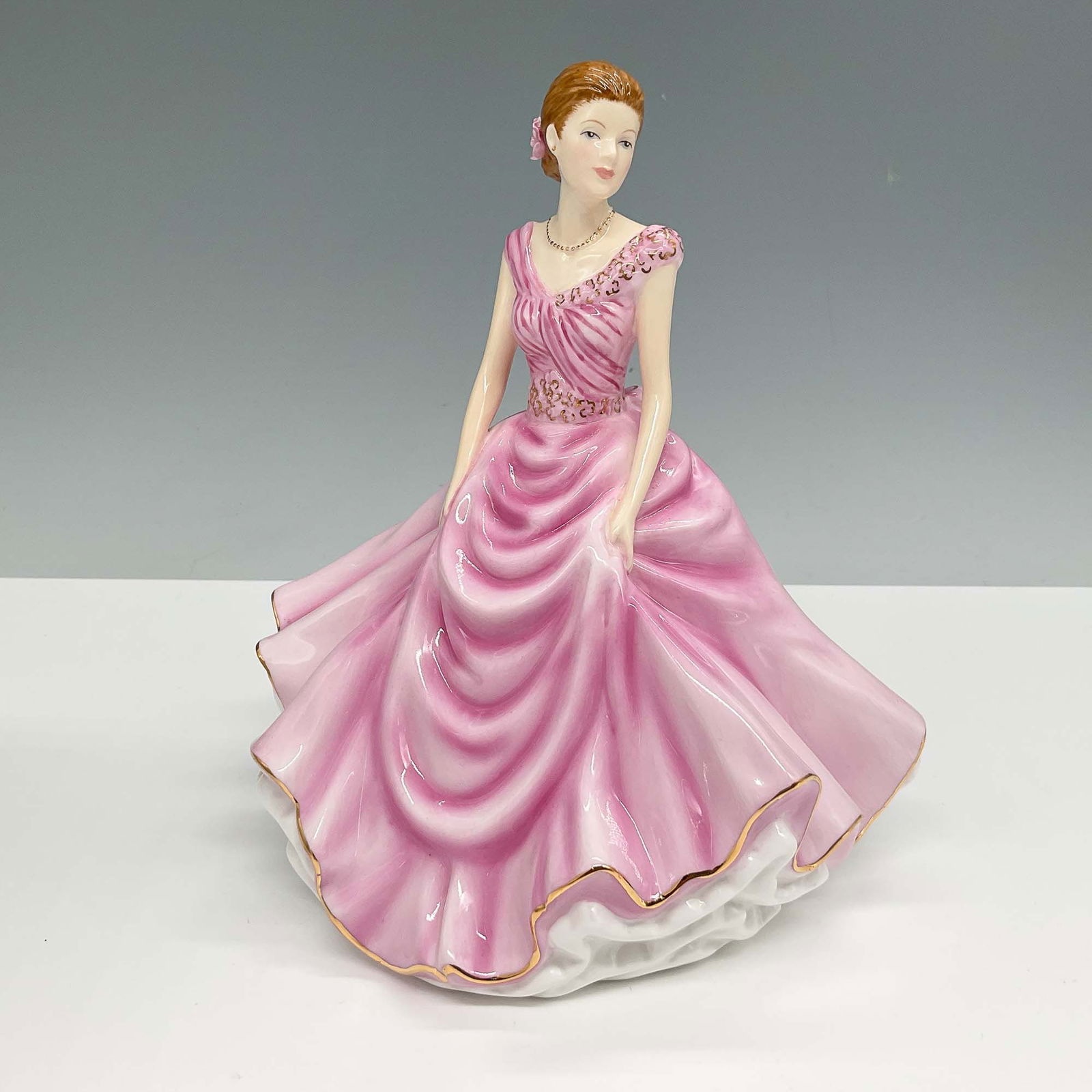Royal Doulton Figurine, Donna HN5590: Royal Doulton porcelain figurine Donna, Petite Figure of the Year 2013, HN5590. Elegantly hand-decorated in bone china, this figurine features a woman in a flowing pink gown with gold trim, adorned wi