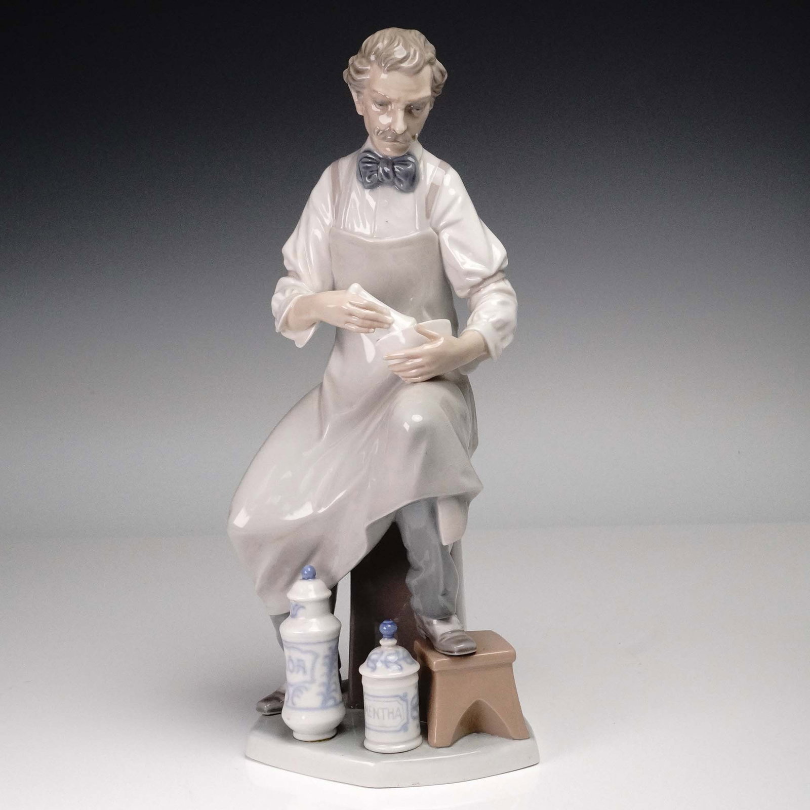 Lladro Porcelain Figurine, Pharmacist 1004844: Beautiful figurine made with subtle colored hues and glossy finish. Lladro backstamp. Artist: Salvador Furio Issued: 1973 - 1985 Dimensions: 4.25"L x 5"W x 12.75"H Country of Origin: Spain