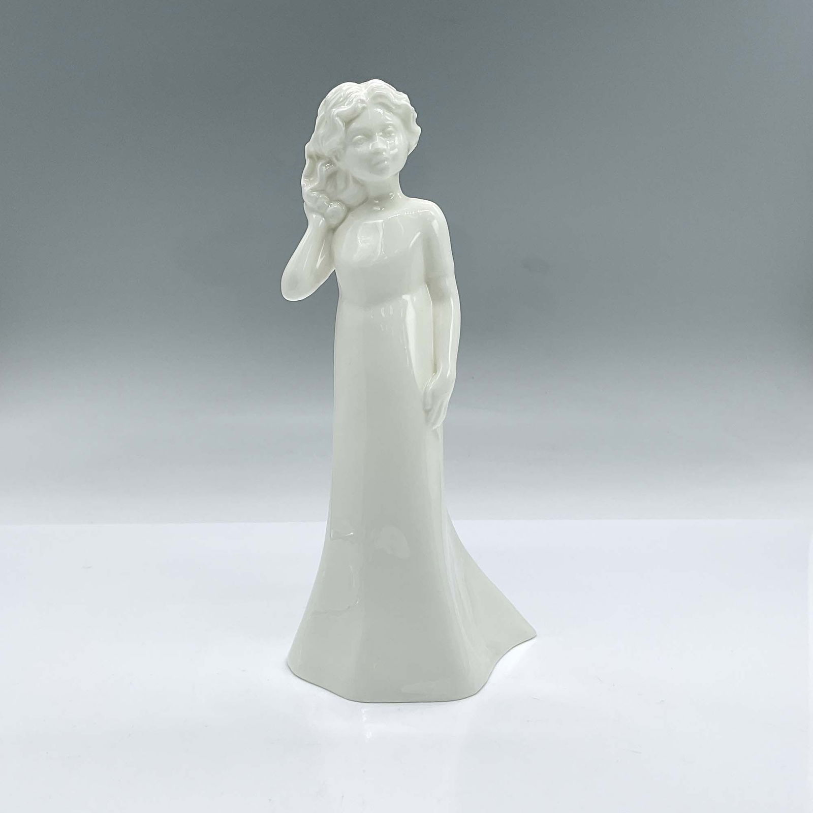 Royal Worcester Figurine, Pretty As A Picture: Glossy solid white bone china figure of a young lady in a long dress sweeping her hair to the right. From the Moments Collection. Royal Worcester backstamp. Issued: 2000 Dimensions: 3.75"L x 3"W x 8"H