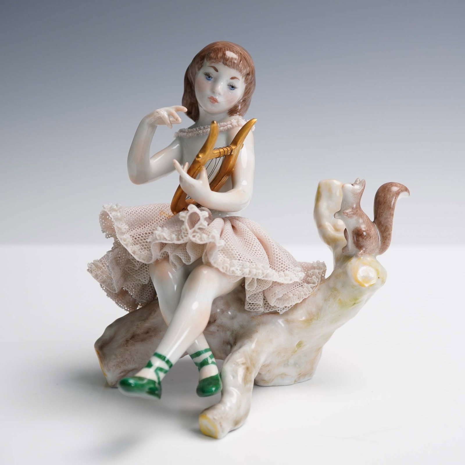 Lladro Porcelain Figurine, Girl with Lyre: This charming Lladro porcelain figurine depicts a young girl seated on a wood-textured log, delicately strumming a handheld lyre while a curious squirrel perches at her side. Hand-painted in soft past