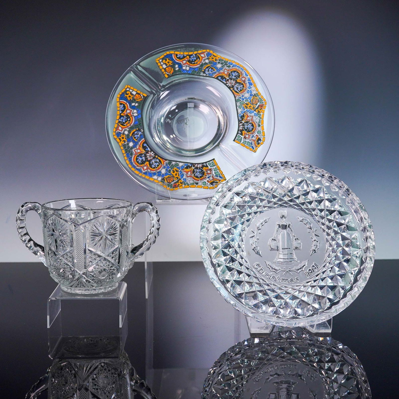 3pc Glass Serveware Lot: This lot comprises a cut-glass handled sugar bowl with double-drop handles and crisp starburst and hobnail cuts; a decorative mosaic glass charger plate featuring a vibrant enamel tessellated pattern