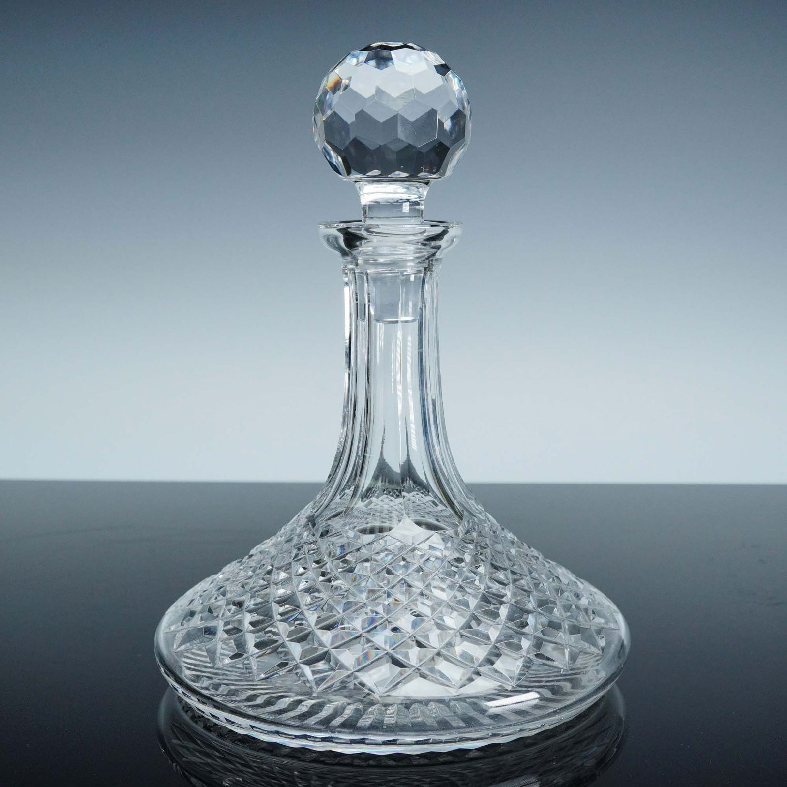 Waterford Crystal Wine Decanter with Faceted Stopper: This elegant Waterford crystal wine decanter features the brand's iconic diamond-cut pattern, extending gracefully across its broad, flattened base and tapering into a smooth, paneled neck. Topped wit