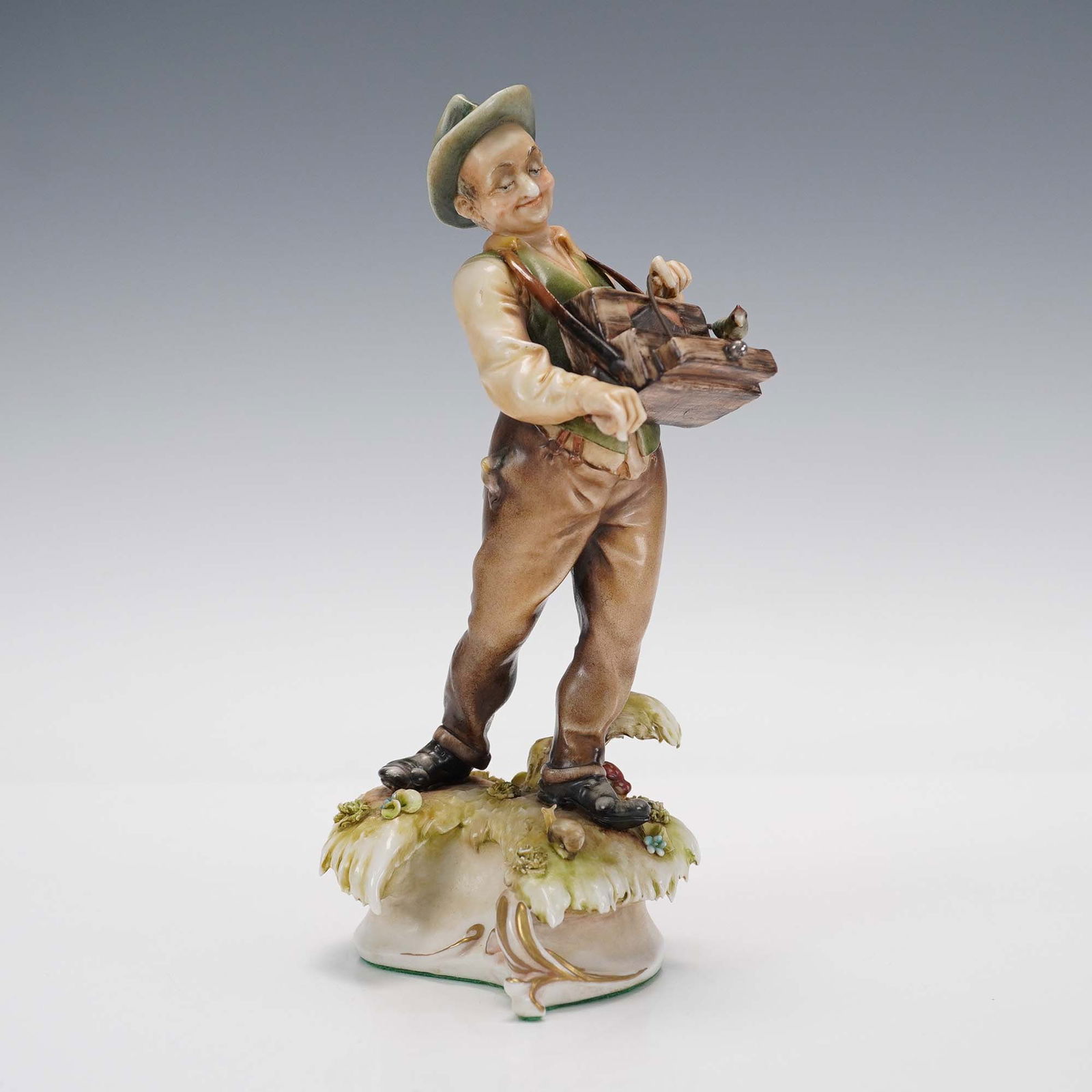 Antonio Borsato Porcelain Figurine, The Organ Grinder: Charismatic porcelain figurine featuring a jovial street performer turning a hand cranked barrel organ with a bird perched on top. Rendered in warm naturalistic tones, the piece captures expressive ch
