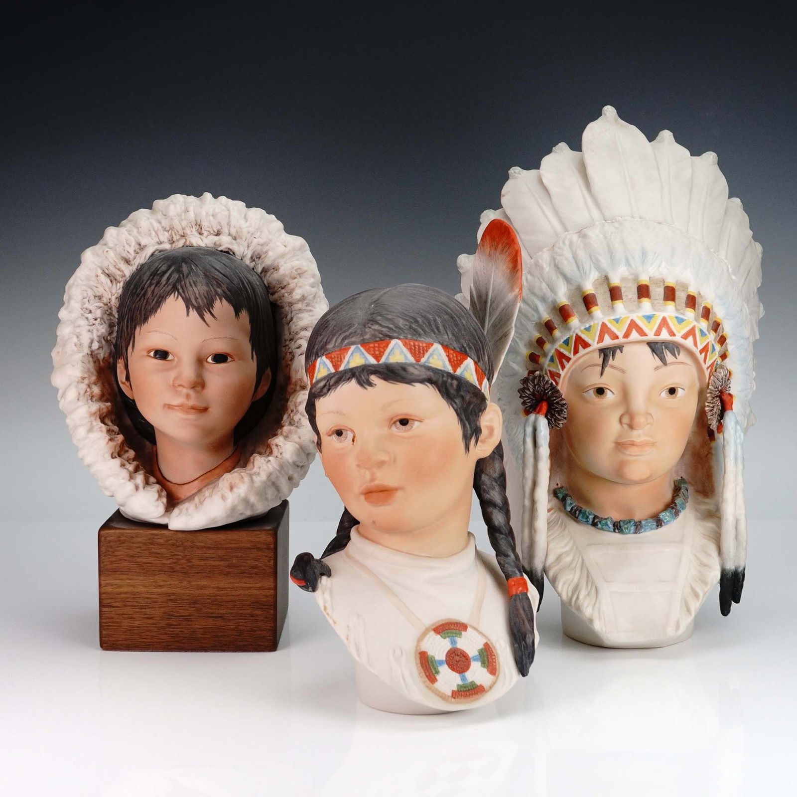 3pc Cybis Porcelain Busts of Native American and Inuit Children: A captivating set of three Cybis porcelain busts portraying children of Indigenous and Inuit heritage. This lot includes: a young girl with braided hair and a feathered headband; a boy in a traditiona