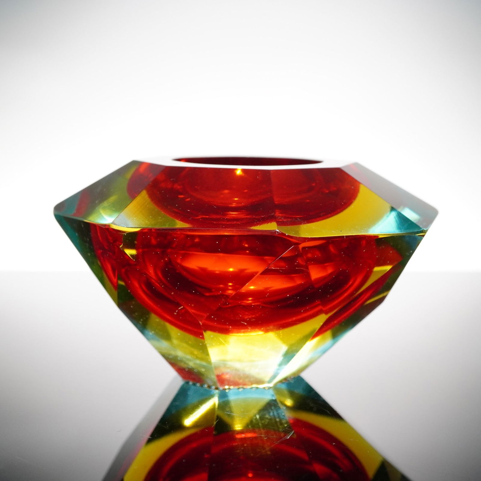 Faceted Murano-Style Art Glass Votive in Amber, Chartreuse & Aqua: A bold and luminous Murano-style faceted glass votive in a mesmerizing tri-color palette of amber red, golden yellow, and aqua blue. Precision-cut and deeply polished, the geometric form radiates with