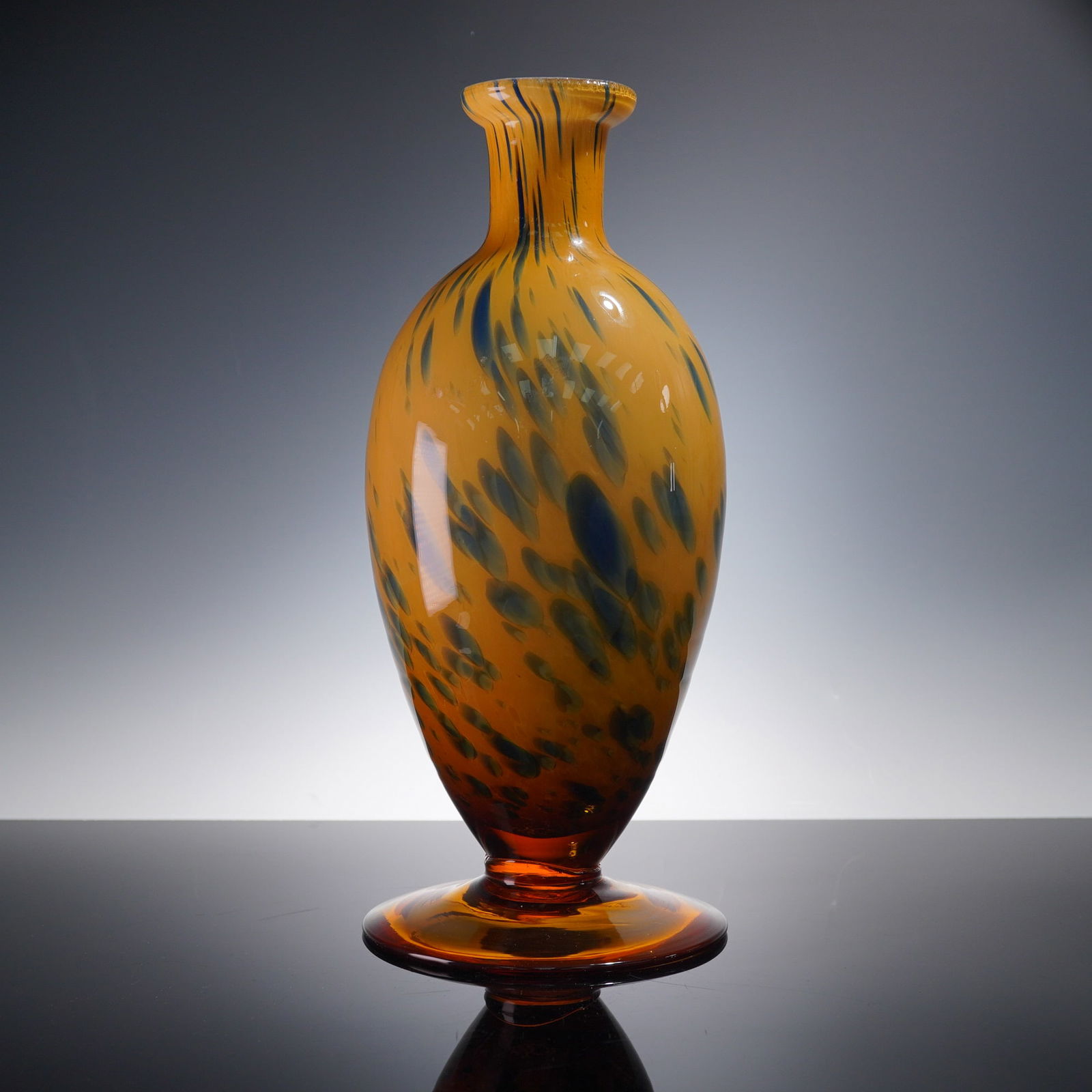 Hand-Blown Art Glass Vase with Amber and Blue Mottling: A tall and elegant hand-blown art glass vase with a rich amber base and striking blue-green mottled inclusions. The elongated ovoid body gracefully rises from a wide circular foot and flares at the co