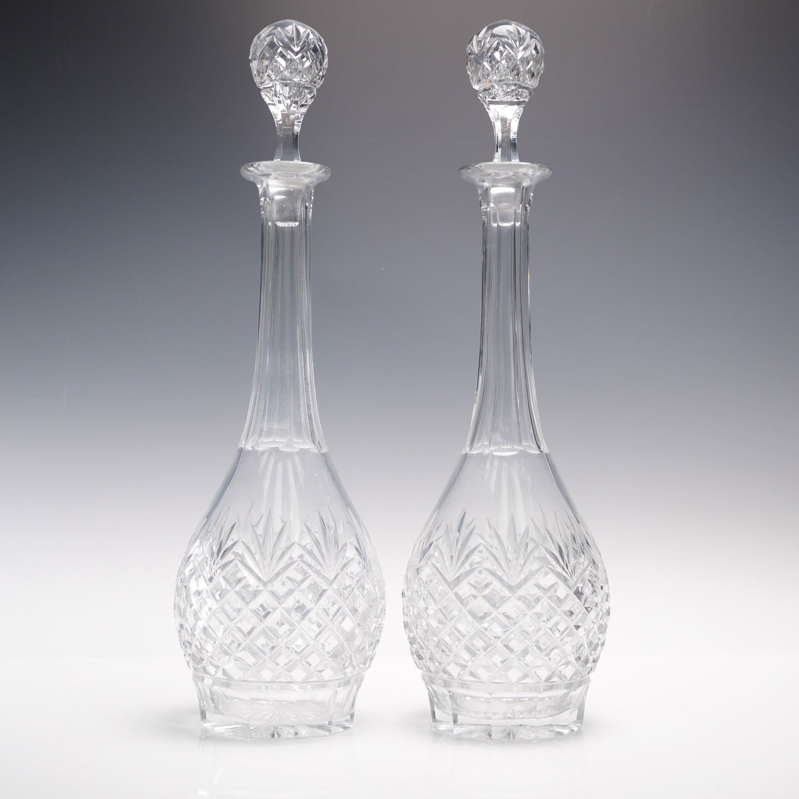 2pc Tall Cut Crystal Decanters with Stoppers: Pair of tall clear cut crystal decanters, each featuring a classic tapered neck and faceted ball-shaped stopper. The bodies are decorated with intricate crosshatch and fan cuts in a traditional diamon