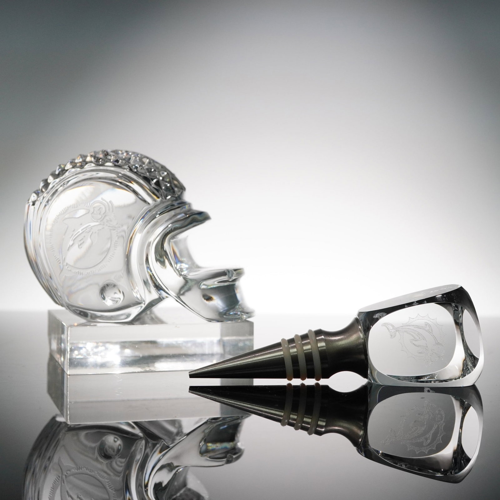 2pc Miami Dolphins Crystal Accessories: Pair of clear crystal NFL collectibles featuring the iconic Miami Dolphins logo: a full football helmet sculpture and a faceted bottle stopper. The helmet is fully rendered in thick, weighty crystal w