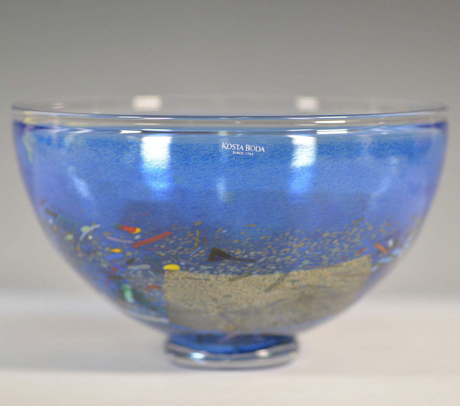 Kosta Boda Bertil Vallien Satellite Art Glass Bowl: A striking Kosta Boda Satellite art glass bowl designed by renowned Swedish artist Bertil Vallien. This expertly crafted piece features a vibrant blue color with abstract multicolored inclusions and m