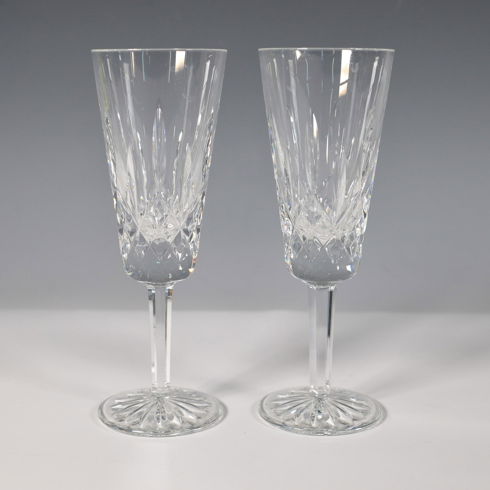 2pc Waterford Crystal Lismore Champagne Flutes: A pair of elegant Waterford crystal champagne flutes in the iconic Lismore pattern, each measuring 7.25"H. Featuring intricate diamond and wedge cuts with a starburst base, these timeless flutes exemp