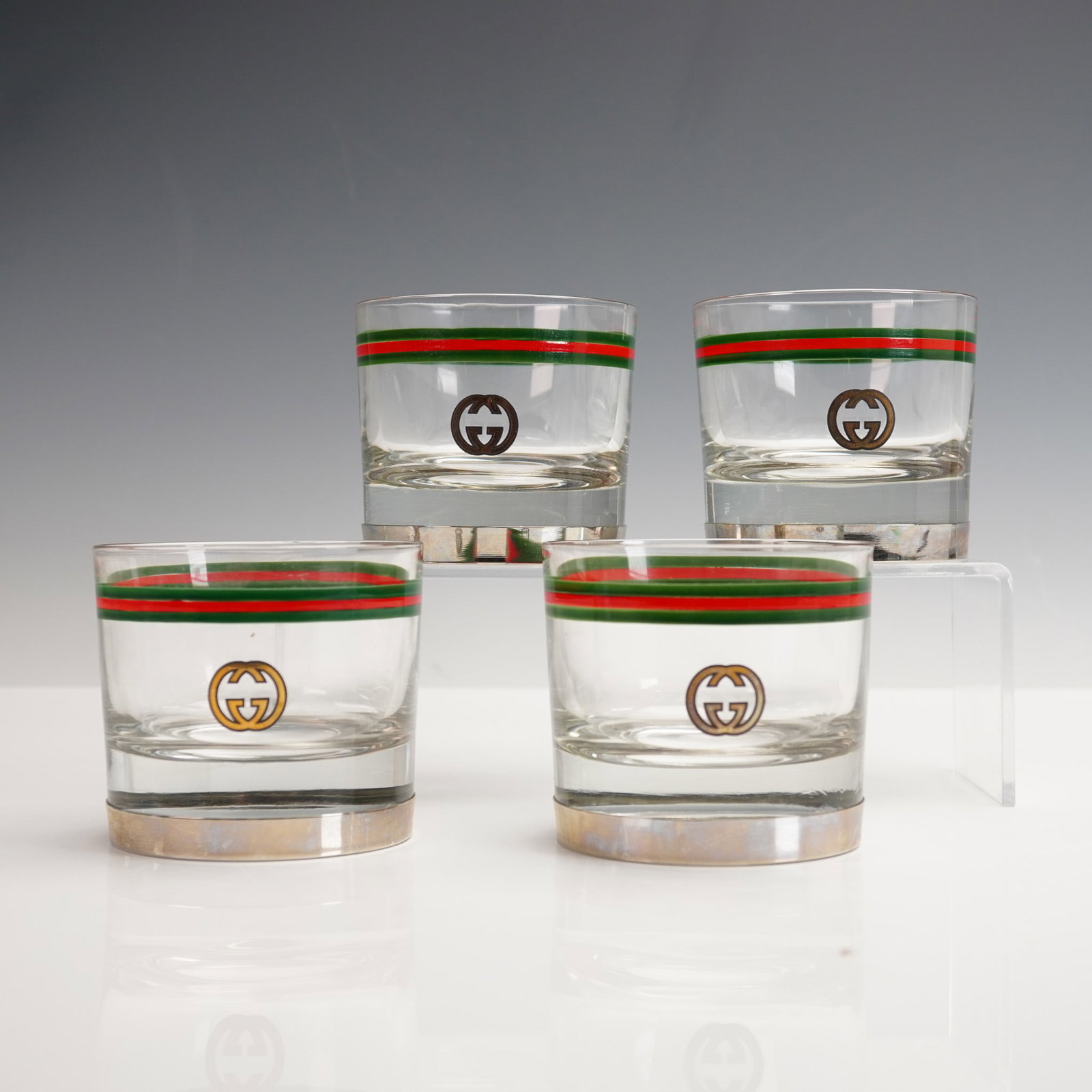 4pc Gucci Old Fashioned Glasses, Green & Red Stripe: A luxurious 4-piece set of Gucci Italy old fashioned glasses featuring the iconic interlocking GG logo and classic green-red-green stripe banding. Each glass is marked "GUCCI ITALY" on the underside. 