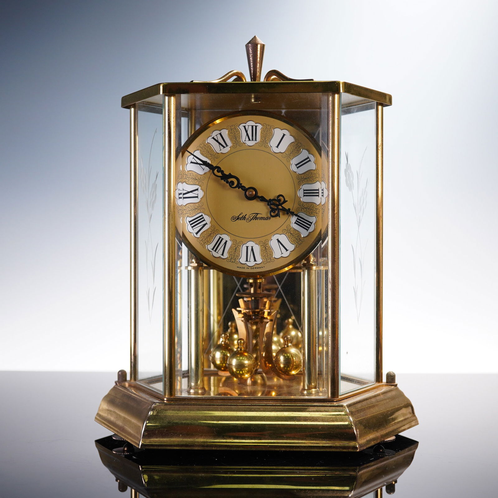 Seth Thomas Bequest Anniversary Clock, Model 0793-000: This elegant Seth Thomas anniversary clock, model number 0793-000, showcases a polished gold-tone glass case with beveled edges and etched floral side panels. The clock features a gold dial with raise