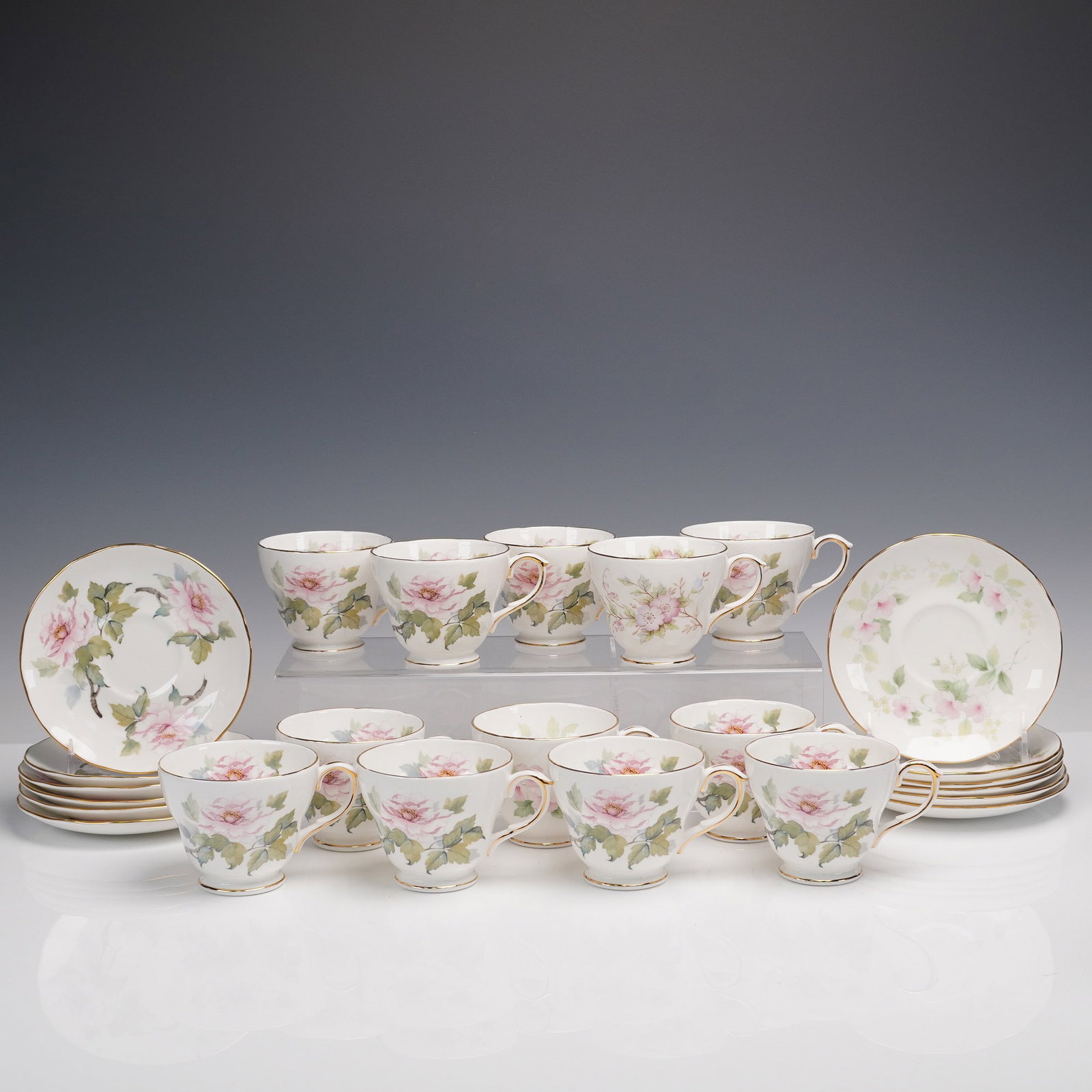 24pc Duchess England Rose Teacup & Saucer Set: Lovely English bone china tea service by Duchess, featuring twelve matching teacups and twelve saucers. Each piece is adorned with soft pink roses and leafy green foliage, finished with delicate gold 