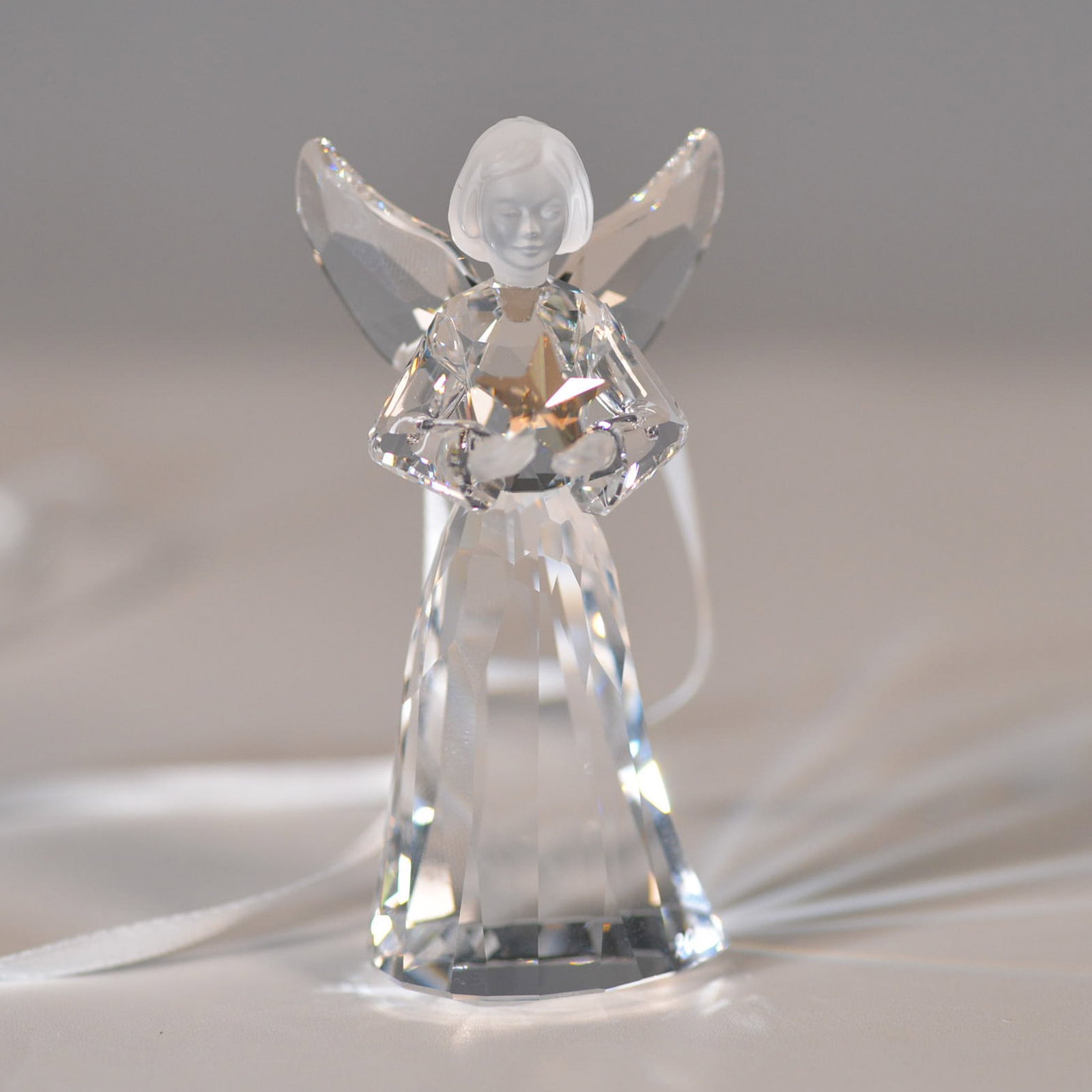 Swarovski Crystal Figurine, Angel Ornament: Swarovski crystal angel ornament featuring a faceted clear crystal body, frosted face, and outstretched wings, holding a gold-tone star. Includes an attached white ribbon for hanging. Comes with the o