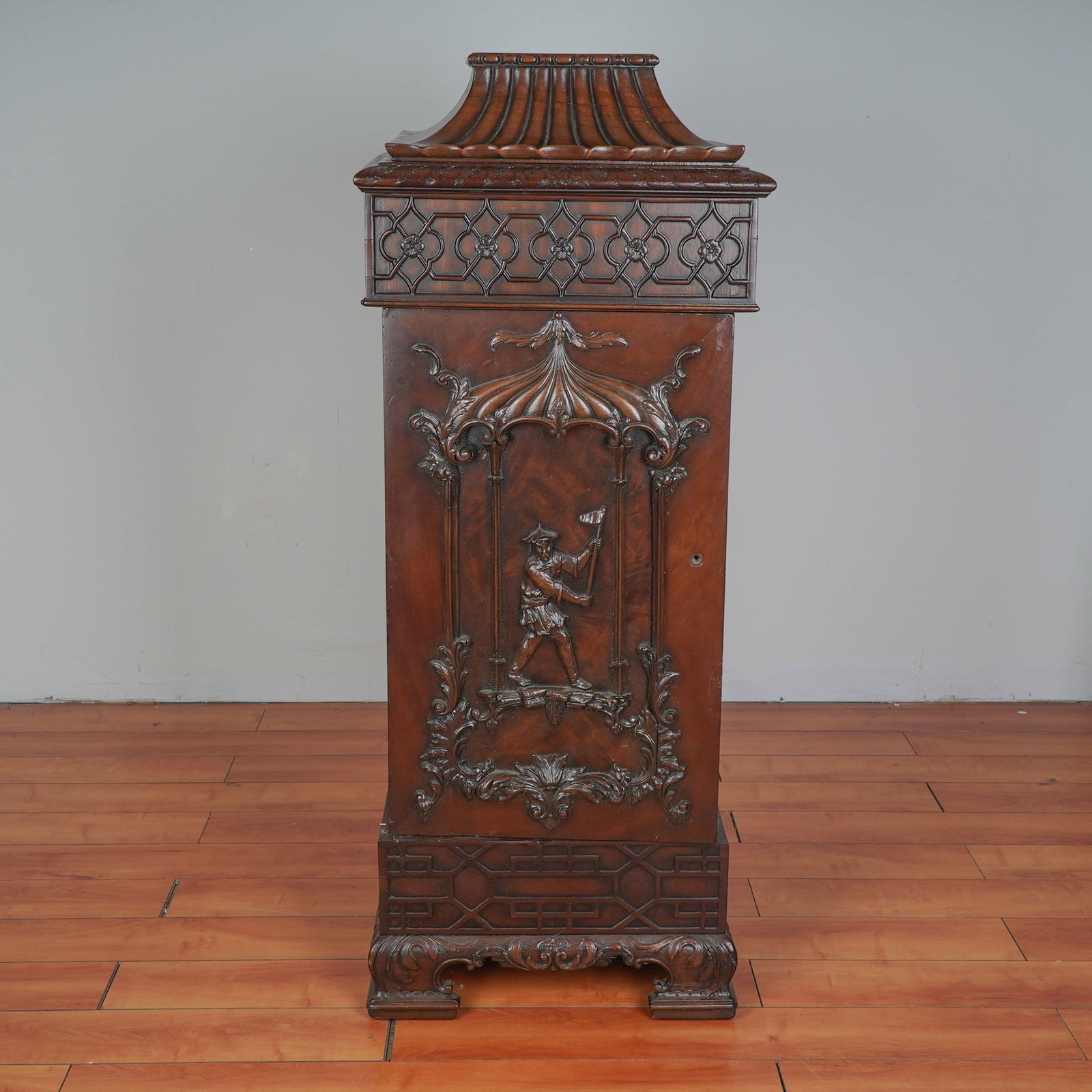 Chippendale Revival Carved Mahogany Pedestal Cabinet: An exquisite pedestal cabinet, masterfully constructed from rich, dark stained mahogany. The uppermost section features a flared pagoda style top above a single drawer with pierced quatrefoil fretwork