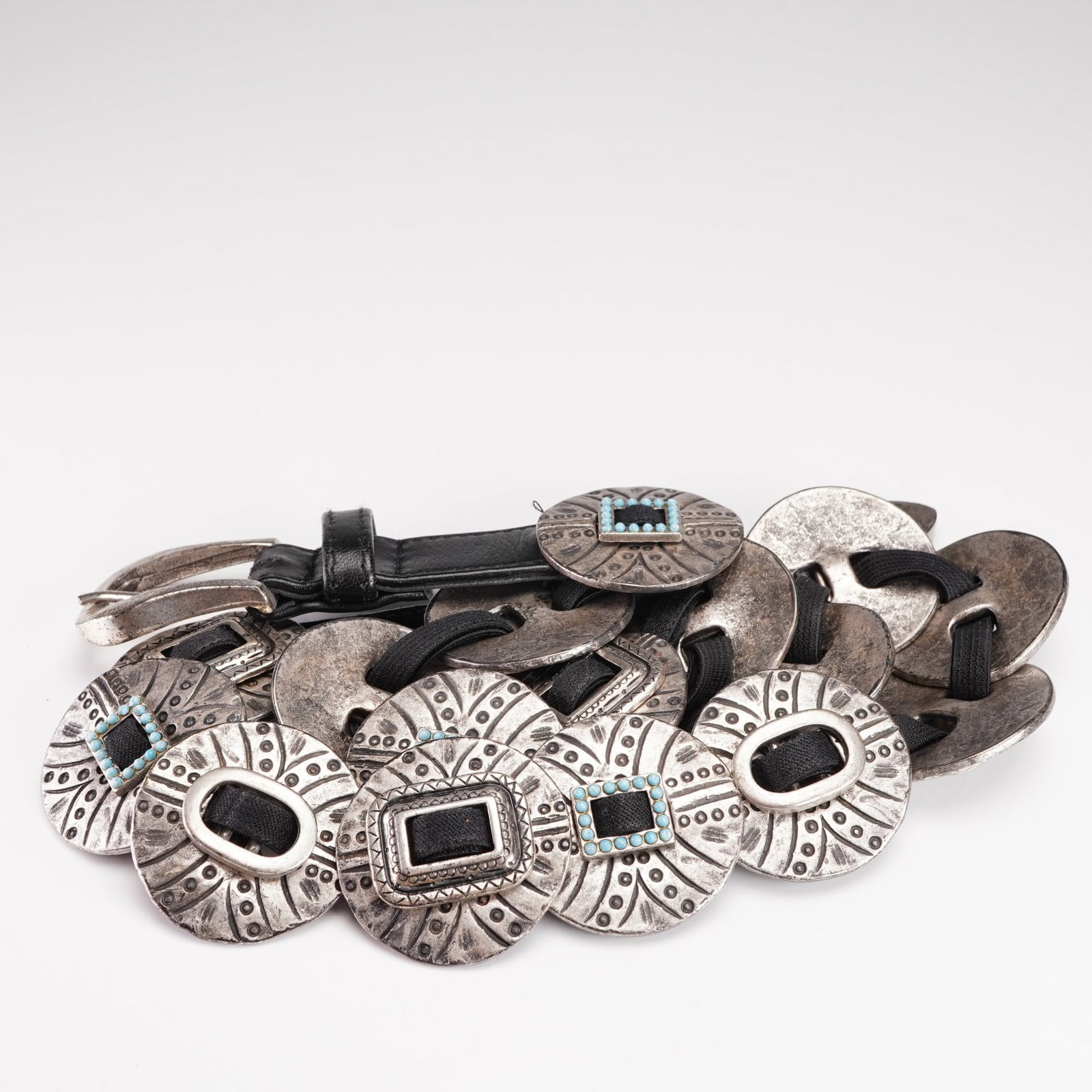 Suzi Roher Black and Metal Concho Belt: A designer concho belt by Suzi Roher of Canada, featuring a series of circular silver-tone metal conchos joined by elastic bands and terminating in leather ends. Each concho is decorated with stamped 
