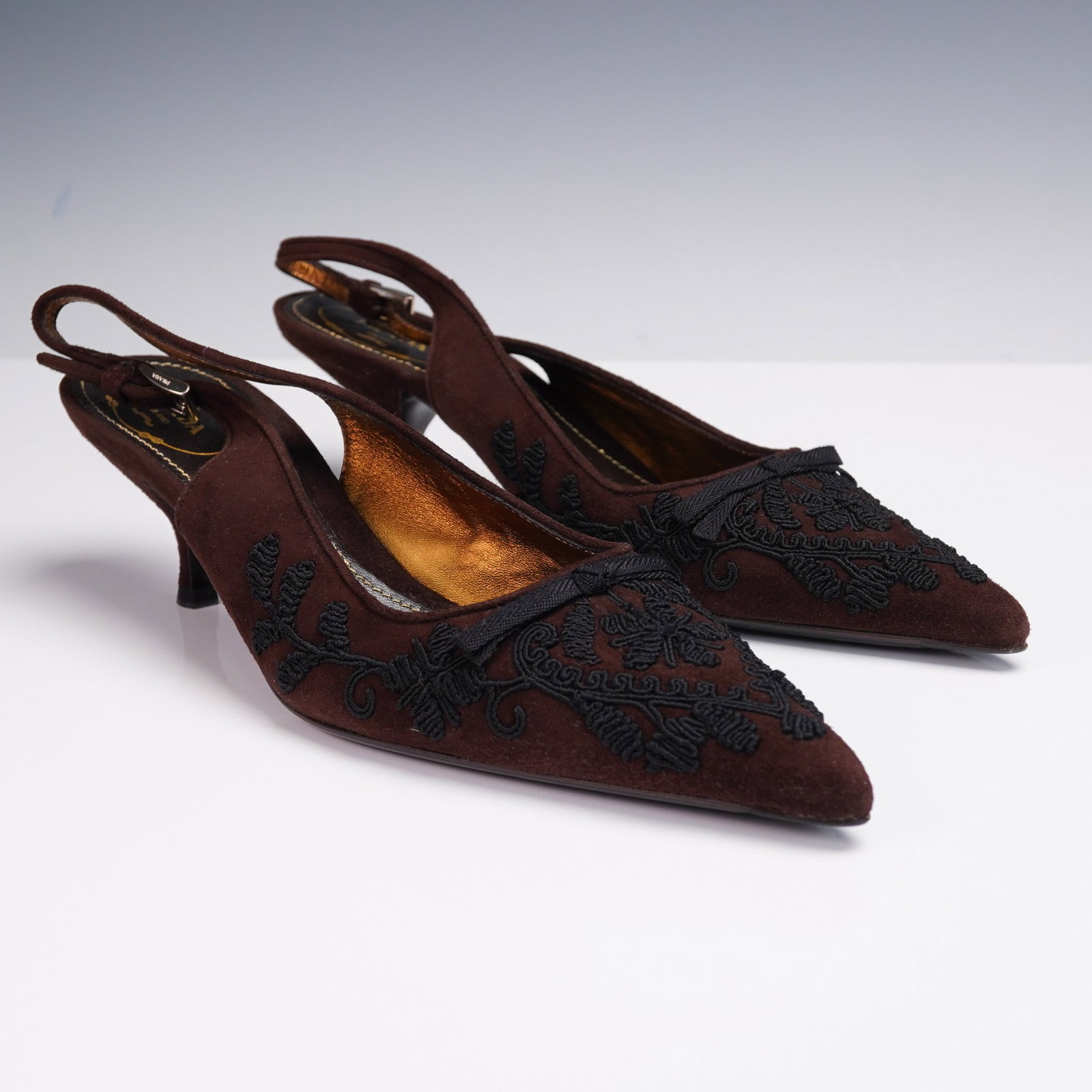 Prada Brown Suede Slingback Heels with Black Embroidery: This elegant pair of Prada slingback heels features a rich brown suede upper adorned with intricate black floral embroidery and a dainty front bow. The pointed toe silhouette is paired with a modest k