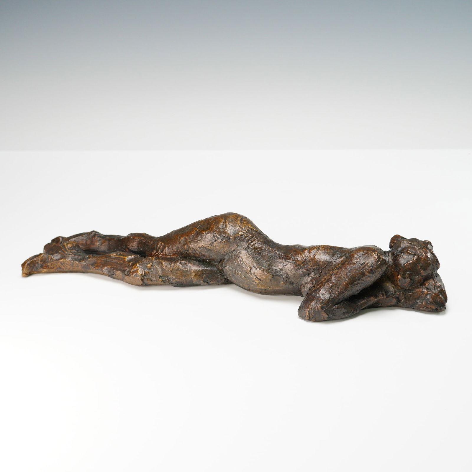 Curt Brill Bronze Figurative Sculpture, Reclining Nude 1996: This limited edition bronze sculpture by American artist Curt Brill depicts a reclining female nude in a tranquil, stretched-out pose, capturing a moment of quiet introspection. Known for his tactile