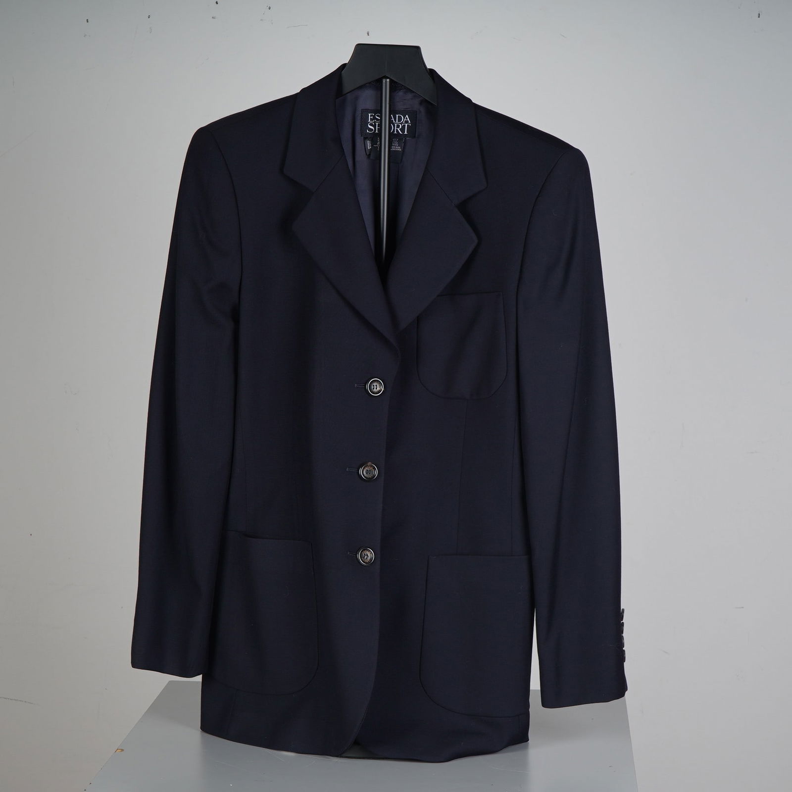 Escada Sport Navy Wool Blazer: Tailored in a rich navy hue, this Escada Sport blazer delivers a modern silhouette with classic sophistication. Expertly crafted from 100 percent virgin wool, it features a three-button front, structu
