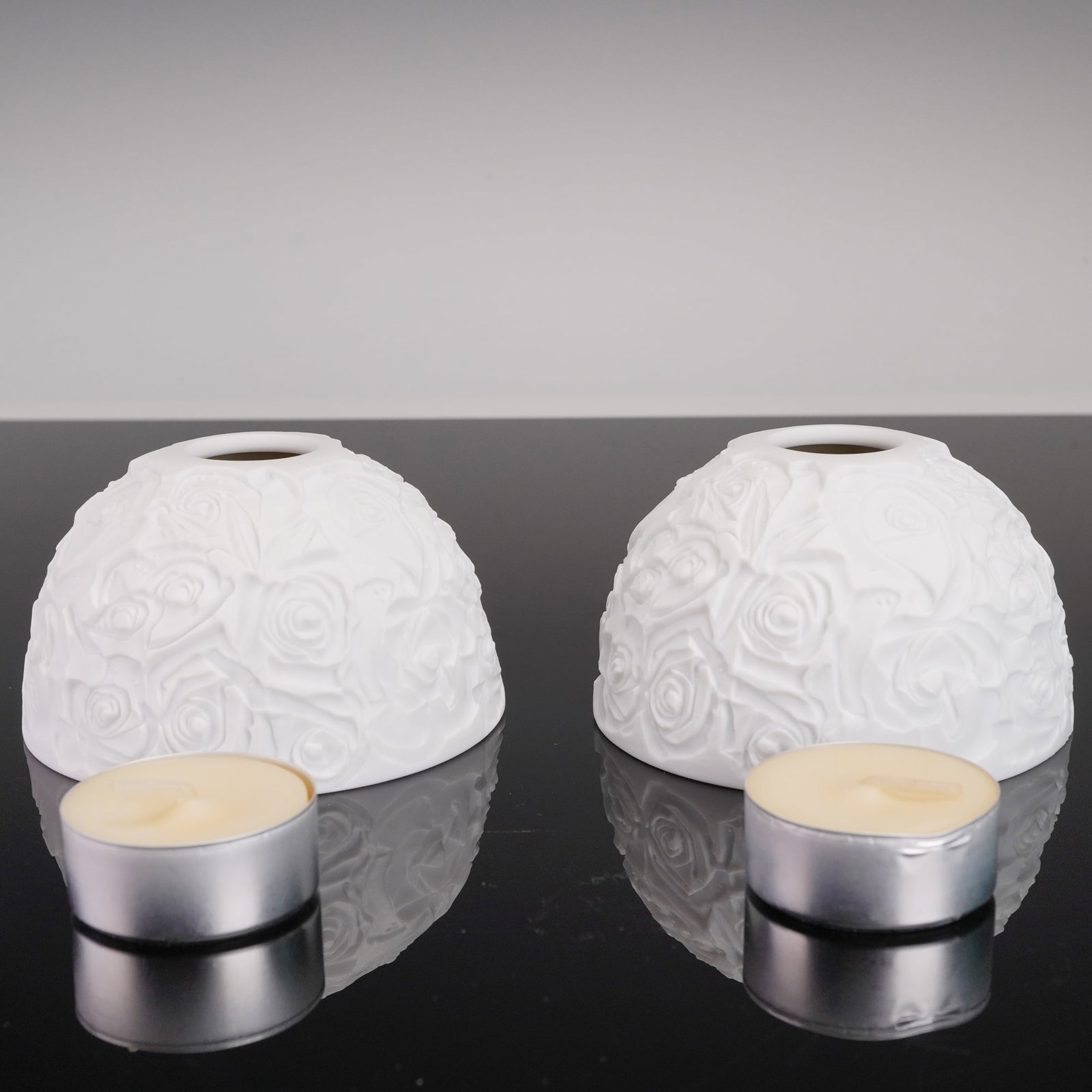 Pair of Bernardaud Bisque Porcelain Votive Candle Holders: Pair of bisque porcelain votive candle holders by Bernardaud, each domed shade featuring a richly textured allover relief of blooming roses. The unglazed finish accentuates the sculptural depth, and w