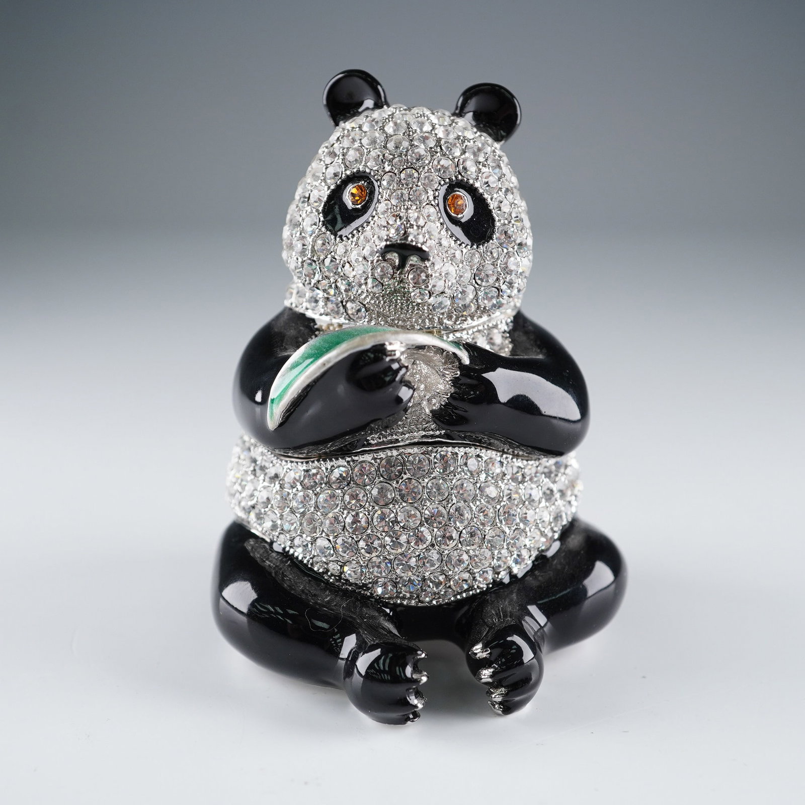 Rucinni Jeweled Panda Trinket Box: Rucinni decorative hinged trinket box in the form of a seated panda bear. The piece is richly embellished with rhinestones across the body and face, accented with bright orange eyes. The body opens on