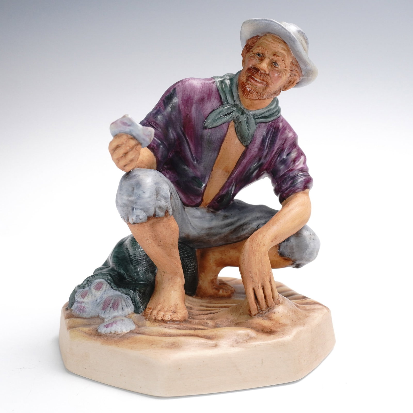 Royal Doulton Figurine, Beachcomber HN2487: Royal Doulton figurine titled Beachcomber, model HN2487, depicting a bearded man crouched on a sandy base, holding a seashell and wearing a wide-brimmed hat, open shirt, and rolled-up trousers. Design