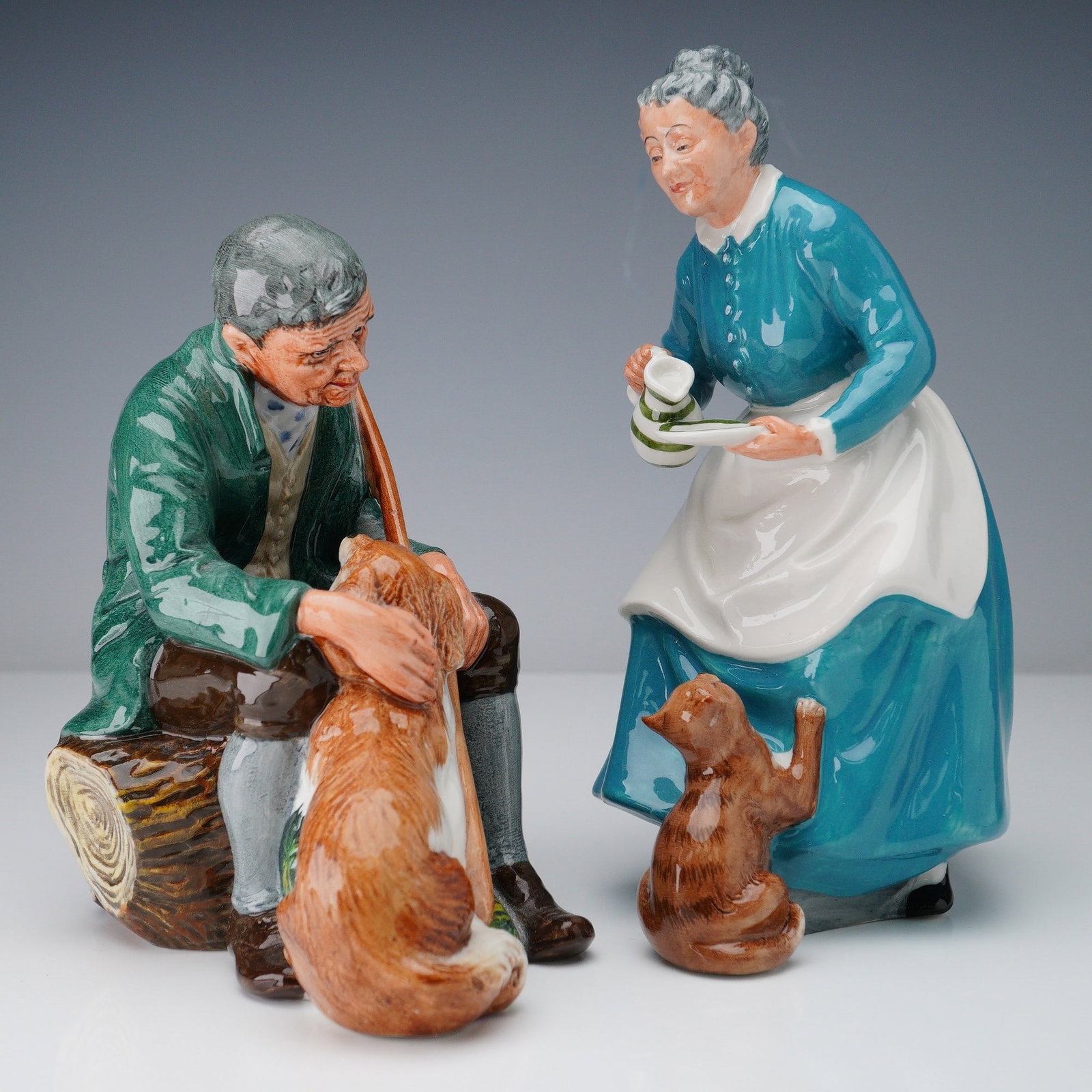2pc Royal Doulton Figurines, The Master and The Favourite: Charming pair of figurines featuring The Favourite HN 2249 and The Master HN 2325. The Favourite depicts a woman offering milk to a kitten, wearing a teal dress and white apron, marked with the 1959 D