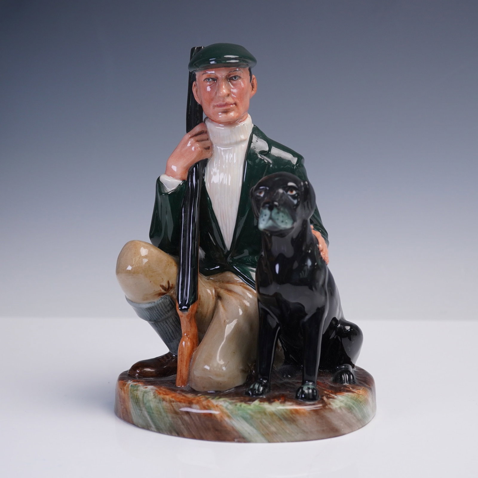 Royal Doulton Porcelain Figurine, The Gamekeeper HN2879: This Royal Doulton porcelain figurine, The Gamekeeper (HN 2879), portrays a poised sportsman kneeling beside his loyal black Labrador, rifle in hand and ready for the hunt. Dressed in a dark green jac