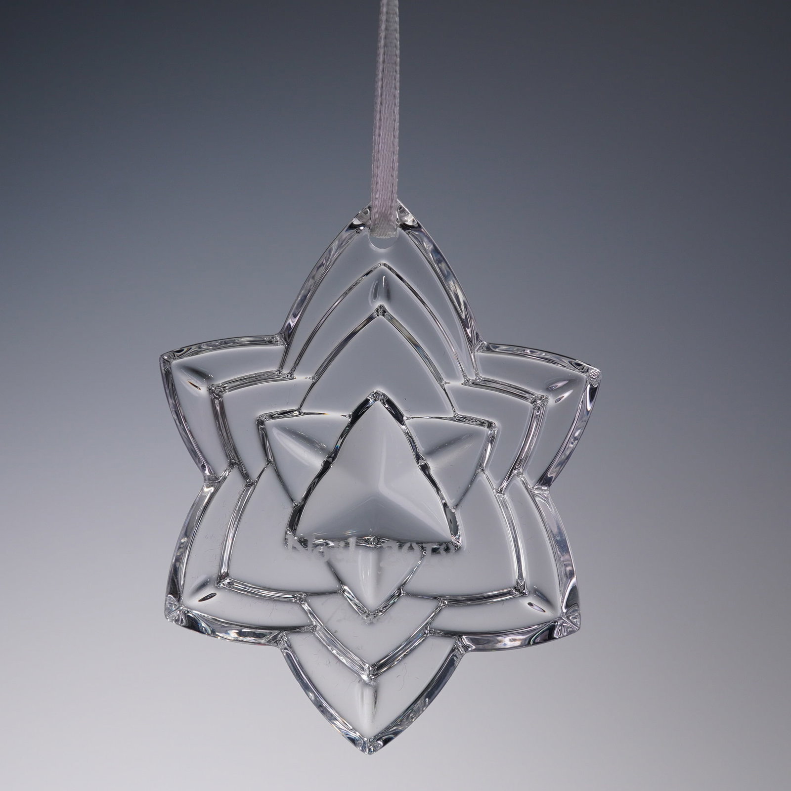 Baccarat Noel 2018 Crystal Snowflake Ornament: A beautifully cut crystal ornament by Baccarat, etched Noel 2018 and Baccarat at the center. This intricate starburst design features layered geometric points and comes suspended from a white hanging 