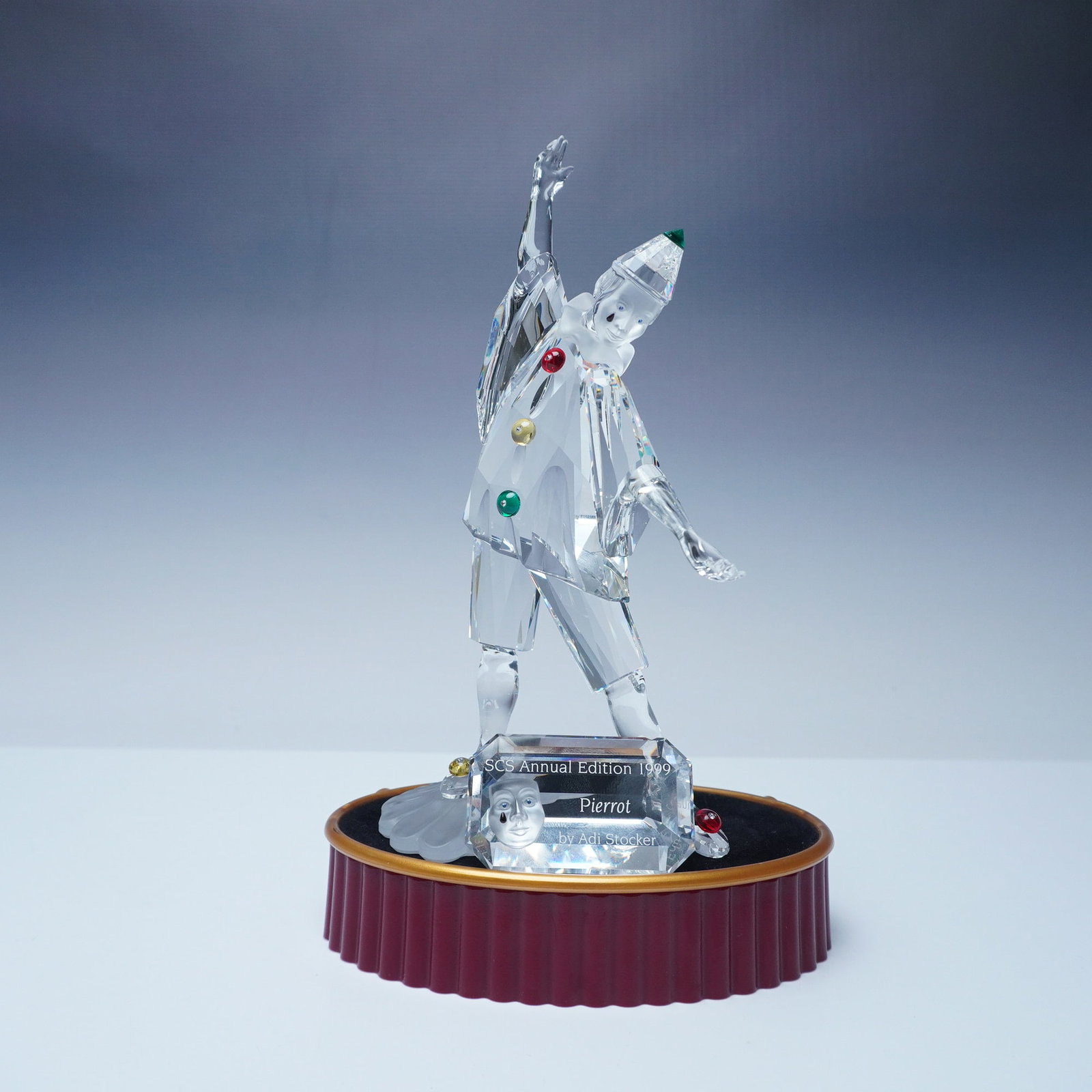 3pc Swarovski Crystal Pierrot Figurine, Plaque & Base: Swarovski SCS Annual Edition 1999 Pierrot, designed by Adi Stocker, from the Masquerade trilogy. This exquisite crystal figurine depicts the classic Pierrot character in a dynamic pose, adorned with m