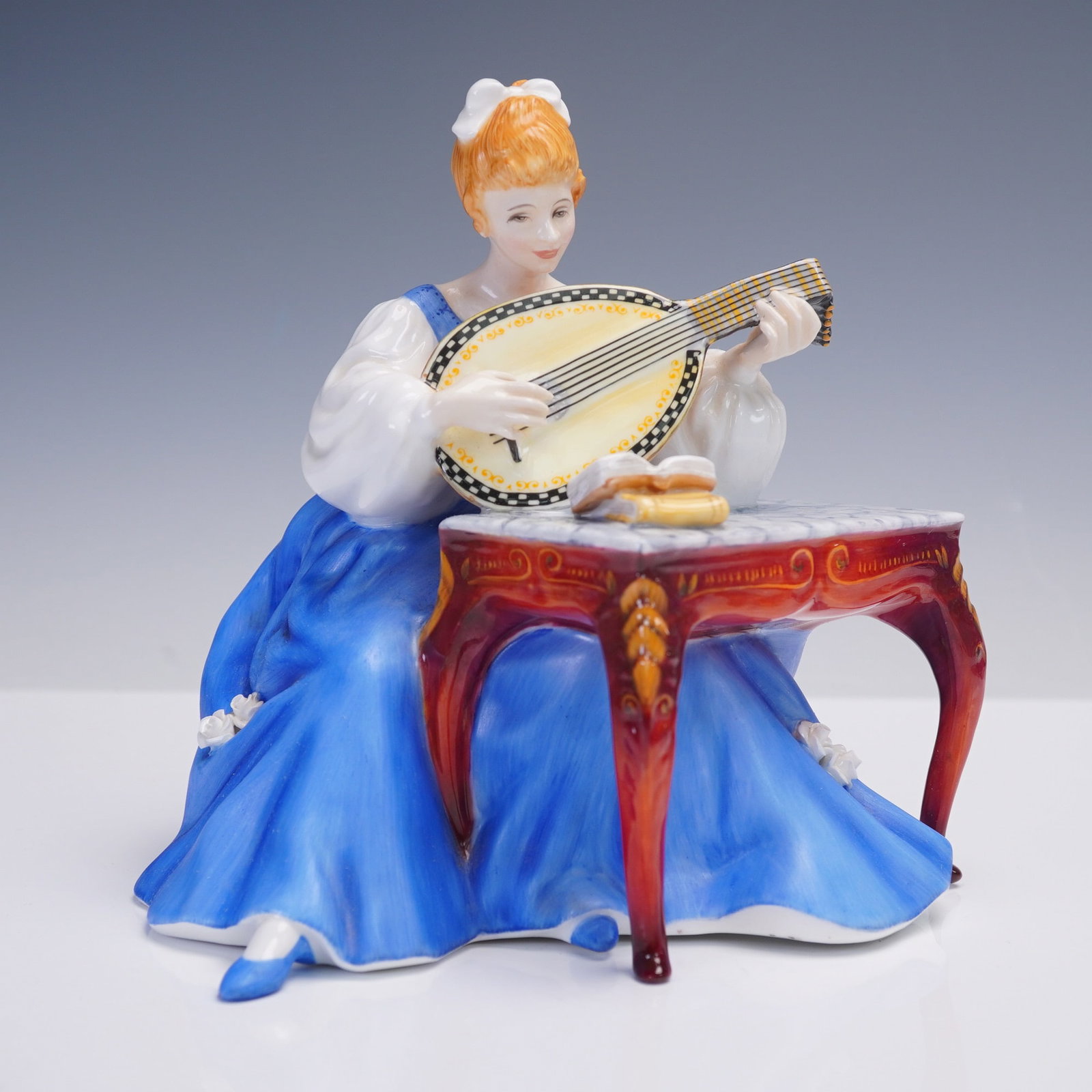 Royal Doulton Figurine, Lute HN2431: Part of the Lady Musicians series introduced in the 1970s, this Royal Doulton figurine titled Lute HN2431 captures a serene moment as a young woman in a flowing blue gown plucks the strings of a class