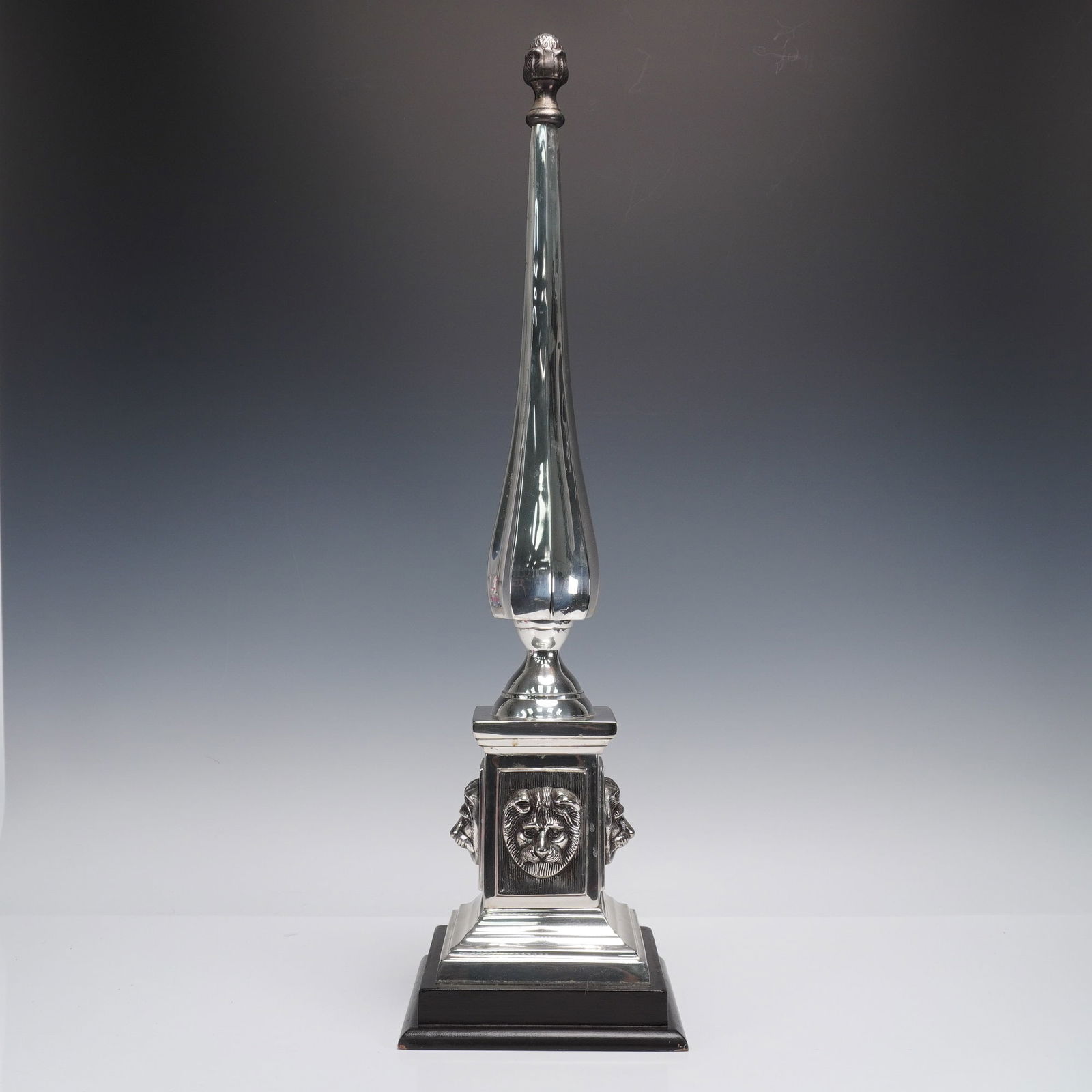 Monumental Silvered Lion-Head Obelisk Finial: An impressive 28-inch decorative obelisk finial, crafted in white metal with a high-polish silvered finish. The tapered body rises to a flamed finial tip and is supported on a stepped square plinth, e