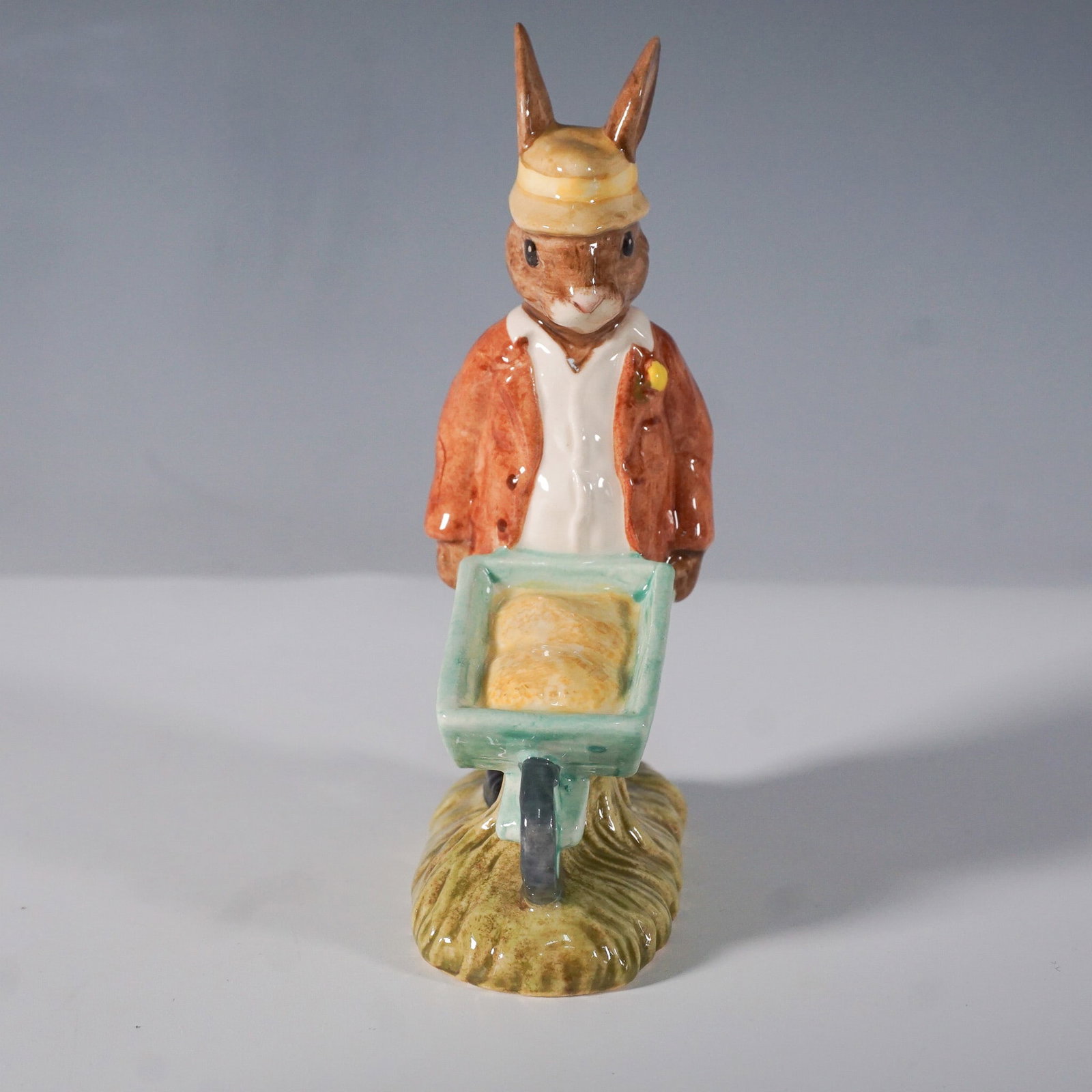 Royal Doulton Bunnykins "Gardener" DB156 Figurine: Charming Royal Doulton Bunnykins Gardener (DB156) figurine, issued between 1996 and 1998. Designed by Warren Platt, it depicts a rabbit gardener in a brown jacket and cap, pushing a green wheelbarrow.