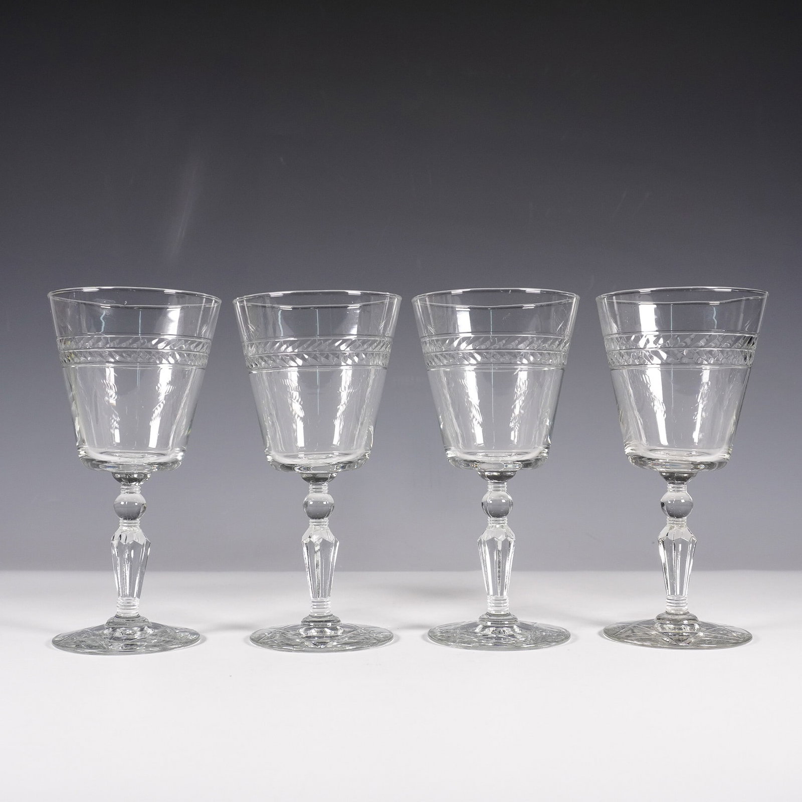 4pc Rock Sharpe Wine Glasses, Jefferson: Set of four clear glass wine glasses featuring a laurel band design encircling the upper portion of each glass. The stems are faceted with a rounded knop detail, leading to a circular base adorned wit