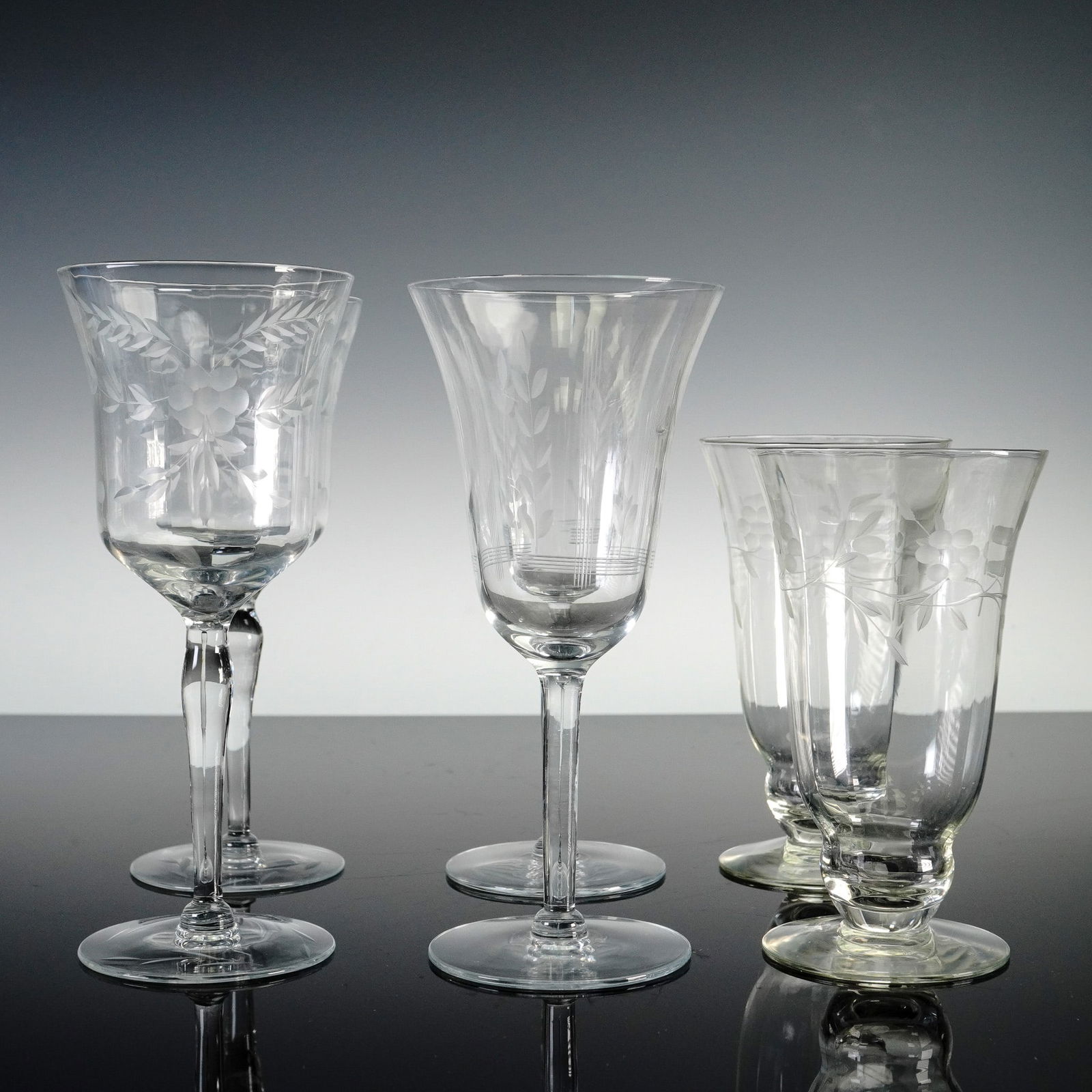 6pc Libbey Glass Company Glass Ware: Assortment of six etched glasses each showcasing variations in floral and foliate etched motifs. The grouping includes two water or wine goblets with etched grapevine designs, two stemmed glasses with