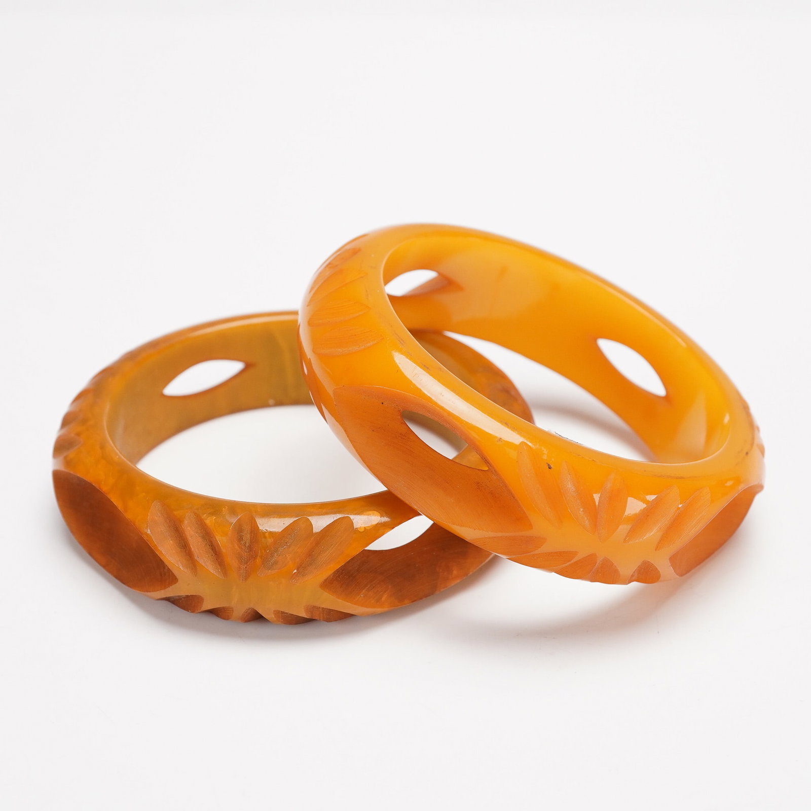 2pc Superb Bakelite Carved Bangle Bracelets: A vintage duo of carved Bakelite bangle bracelets showcasing warm marbled amber and butterscotch tones. Each bracelet is adorned with a deeply incised leaf or floral motif and symmetrical openwork cut