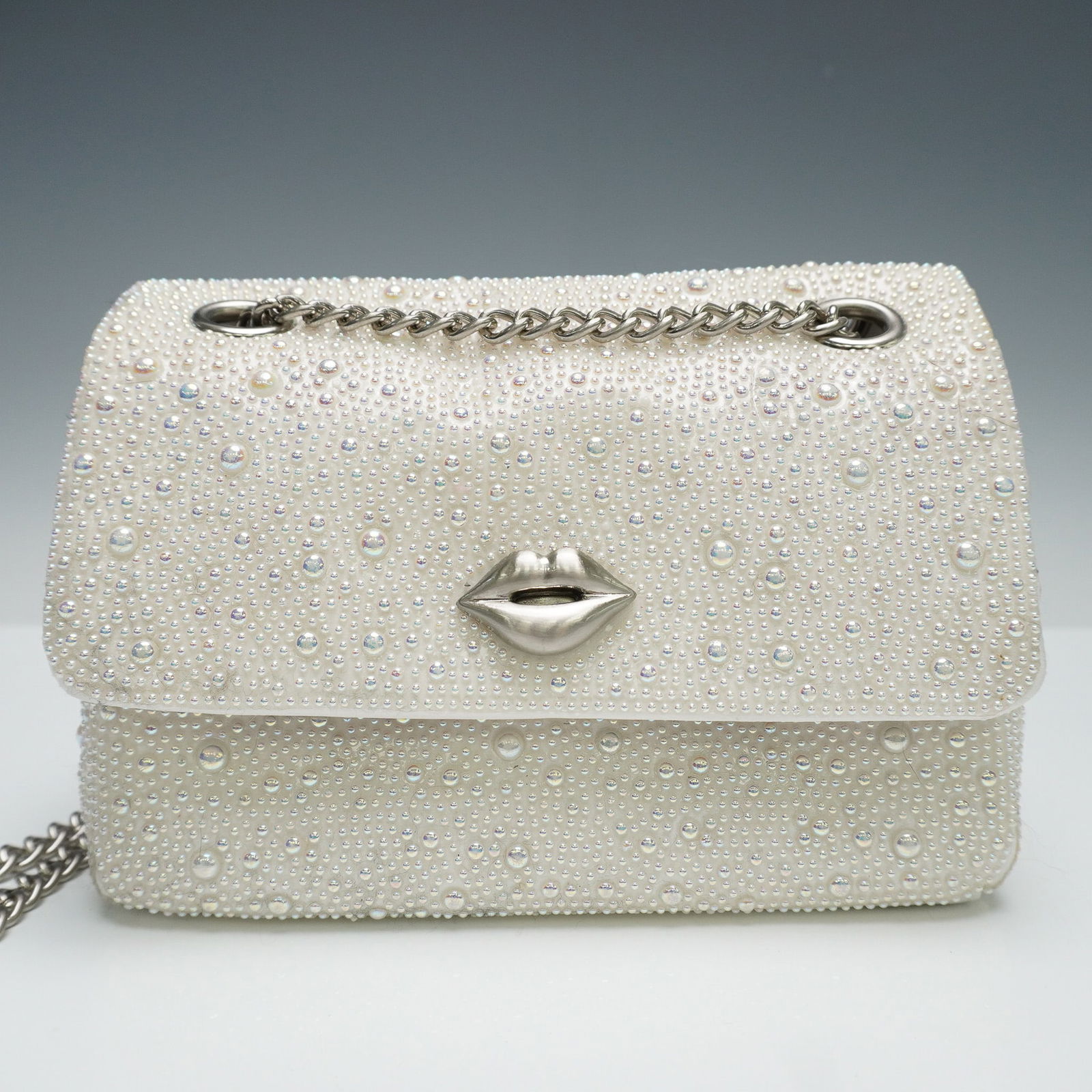 Betsey Johnson White Beaded Crossbody Bag with Lips Clasp: This Betsey Johnson crossbody bag offers a glamorous twist on classic white with an all-over design of shimmering seed beads and faux pearls in iridescent finishes. The front flap is secured by a scul