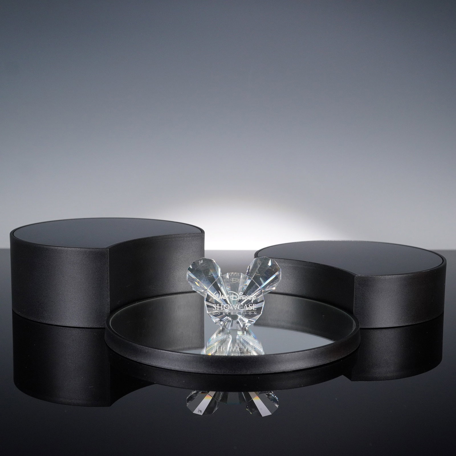Swarovski Crystal Disney Showcase Paperweight with Display: Swarovski crystal paperweight from the Disney Showcase Collection featuring a faceted Mickey Mouse silhouette in the shape of a sparkling three-lobed emblem. The crystal is engraved with the Walt Disn