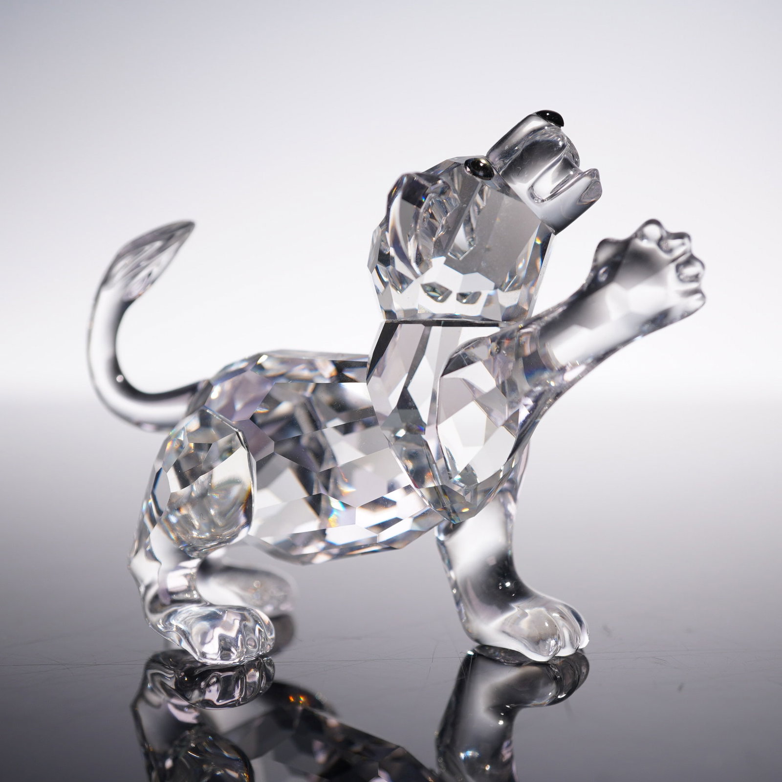 Swarovski Crystal Figurine, Lion Cub: Swarovski crystal figurine depicting a playful lion cub in a dynamic, upright pose. Crafted in precision-cut clear crystal with black iridescent eyes and a black nose. The figure exhibits a beautifull