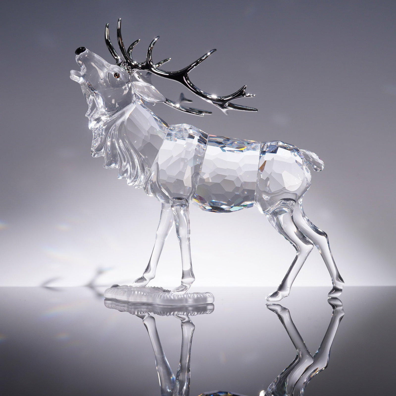 Swarovski Crystal Figurine, Stag: A finely crafted Swarovski crystal stag figurine designed by Adi Stocker, model number 291431. This elegant sculpture features faceted clear crystal with detailed chrome-finished antlers and expressiv