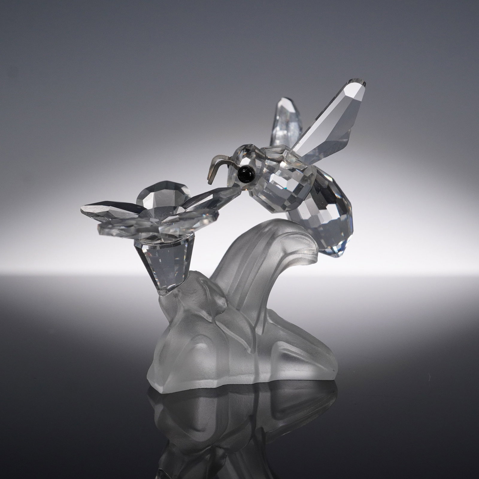 Swarovski Silver Crystal, Bumble Bee on Flower, 166185: This exquisite Swarovski Silver Crystal figurine features a beautifully faceted bumble bee mid-flight, hovering over a delicate flower bloom, both expertly crafted from clear crystal. The bee is perch