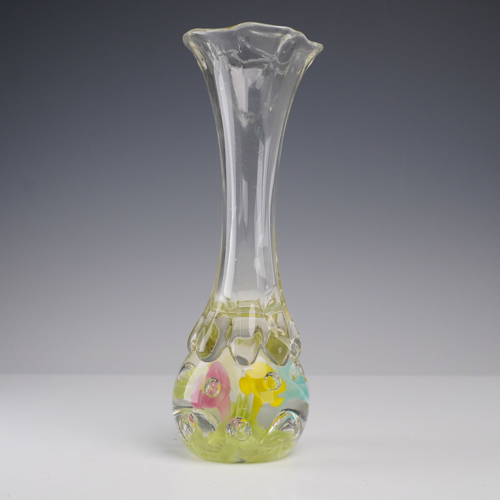 Art Glass Vase with Internal Floral Decoration: Handcrafted blown art glass vase featuring a tall flared rim and bulbous base. The base is infused with internal pastel floral motifs in pink, yellow, blue, and white, rising from a green leafy base. 
