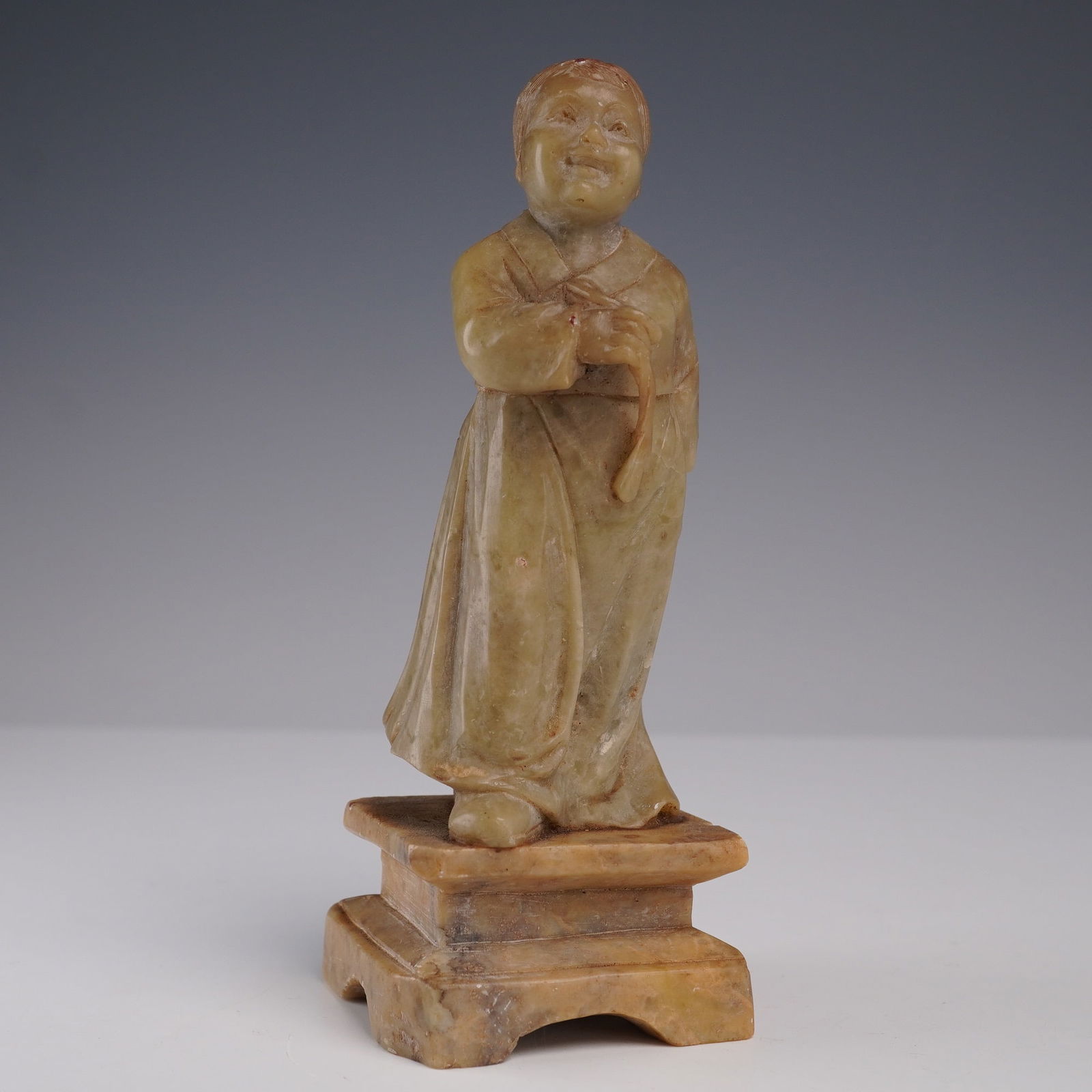 Soapstone Carved Figurine of Woman in Traditional Robe: Carved soapstone figurine depicting a woman in traditional East Asian attire, standing atop an integral square plinth base. The figure wears a long robe with smooth drapery and modest detail, her hand