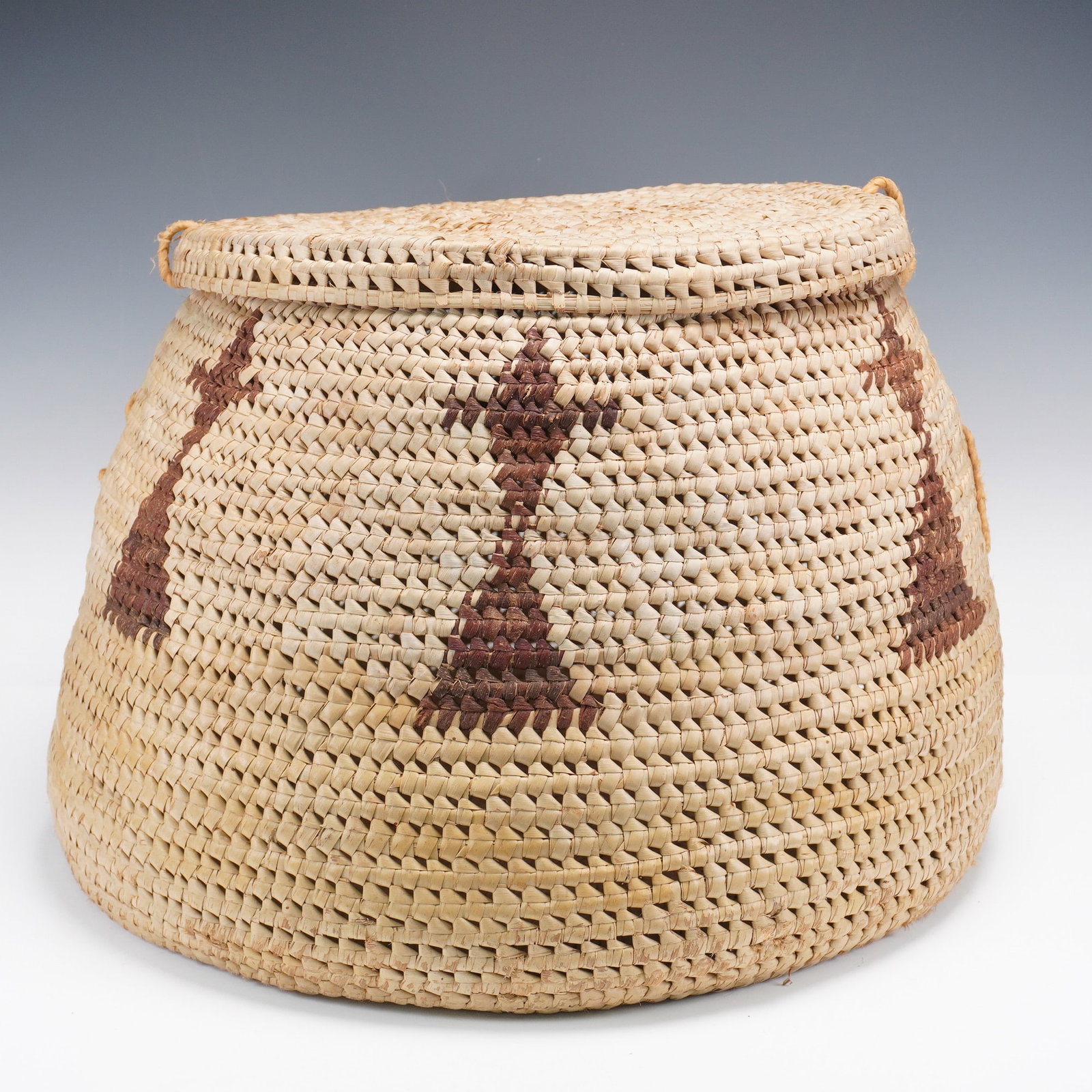 Monumental Native American Lidded Basket with Geometric Motifs: This impressively large Native American lidded basket stands out for both its scale and craftsmanship. Handwoven from natural plant fibers using a tight coiled technique, the basket features repeating