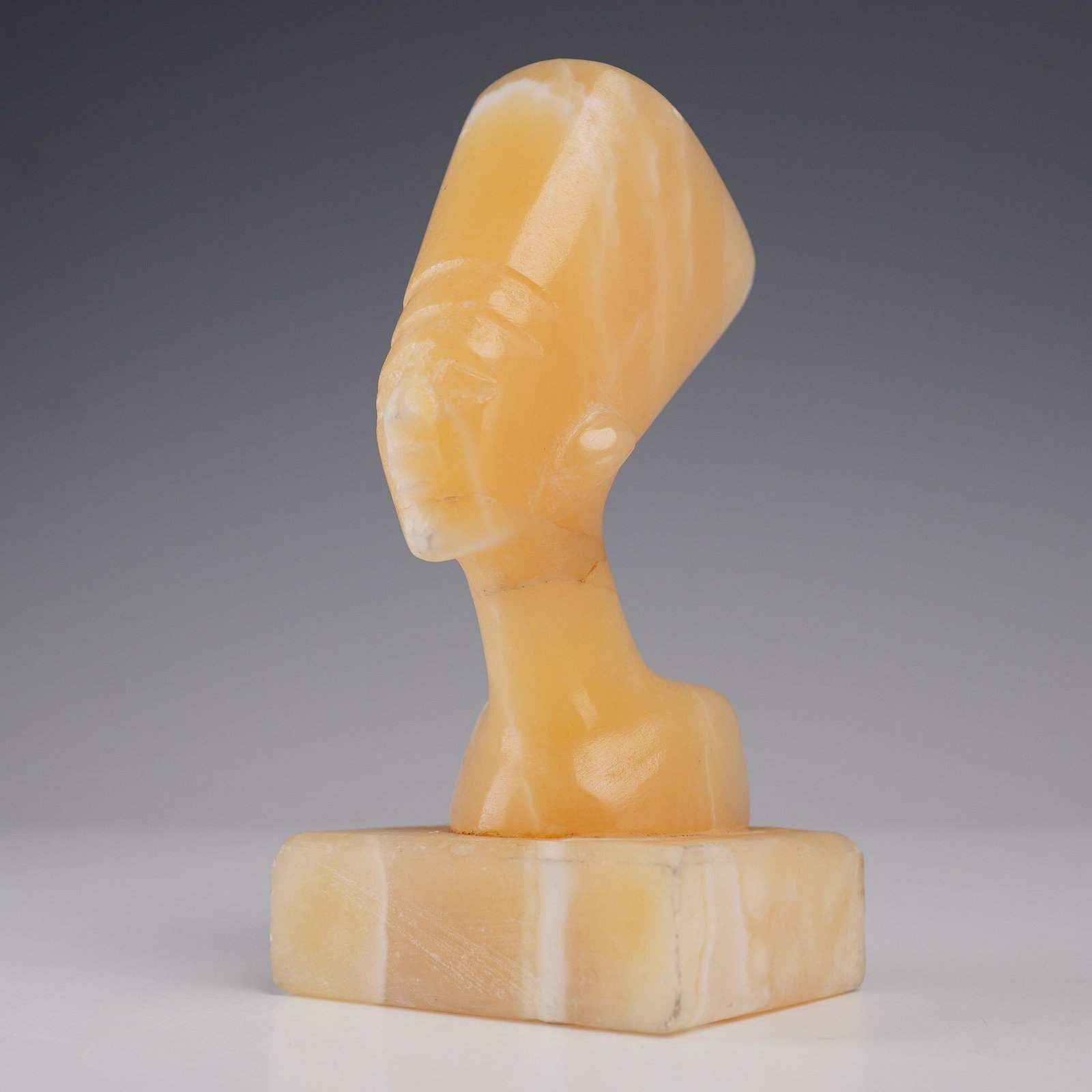 Alabaster Carved Bust, Queen Nefertiti Style: Carved from a warm golden alabaster stone, this stylized bust depicts Queen Nefertiti in profile, showcasing her iconic tall headdress. The piece features smooth lines and subtle facial detail, mounte